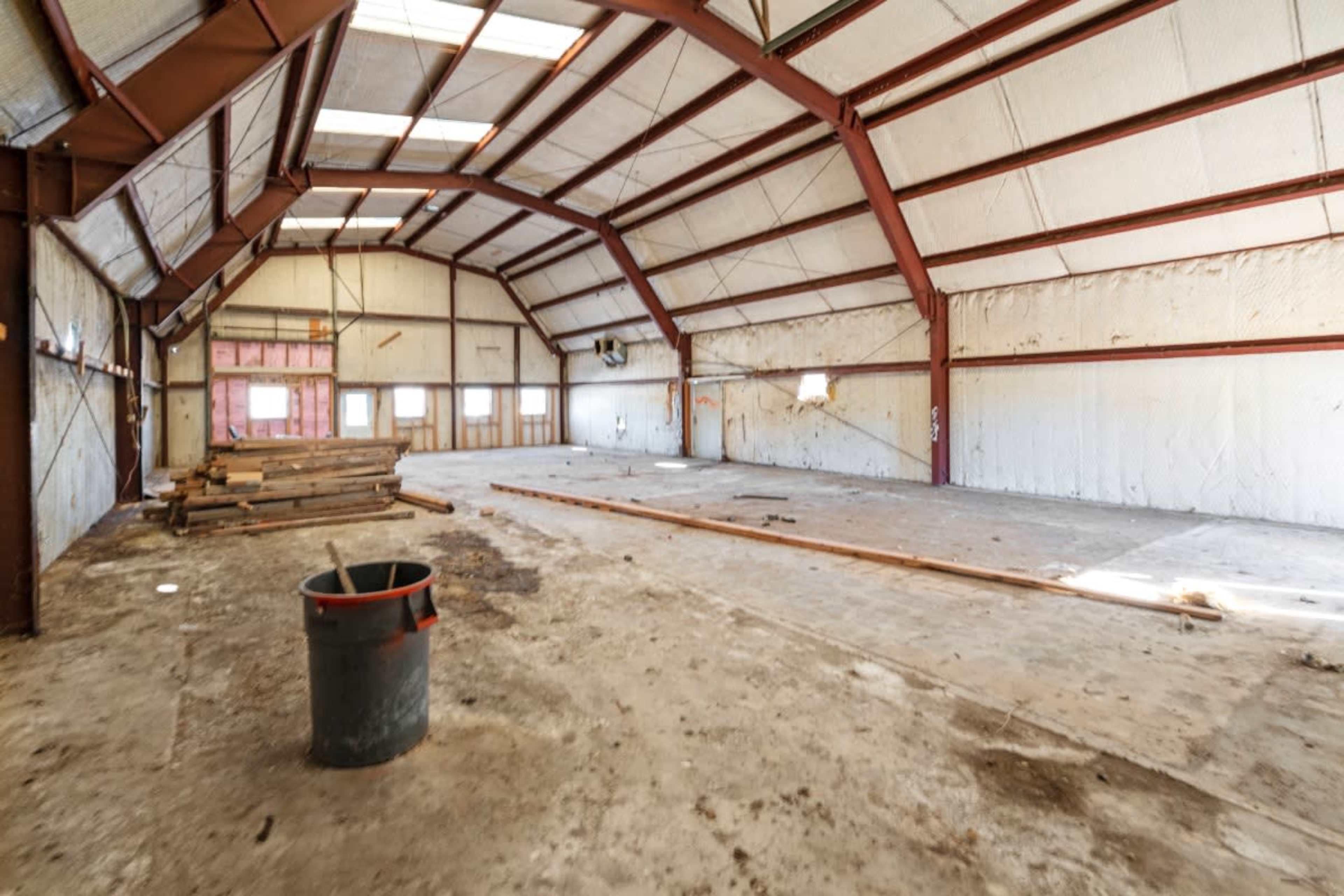 The image shows a large, empty warehouse with exposed metal beams and a concrete floor.