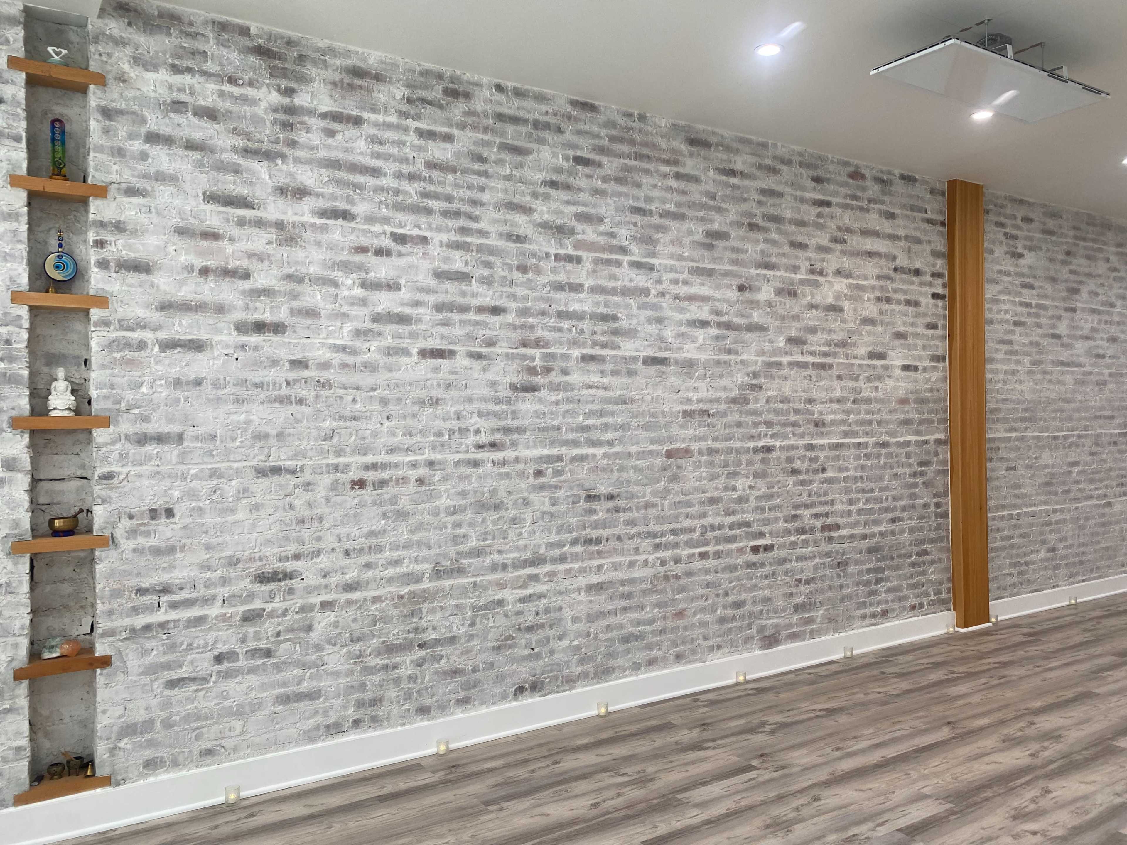 An interior space with a textured white brick wall, accented by wooden shelves on one side and a hardwood floor.