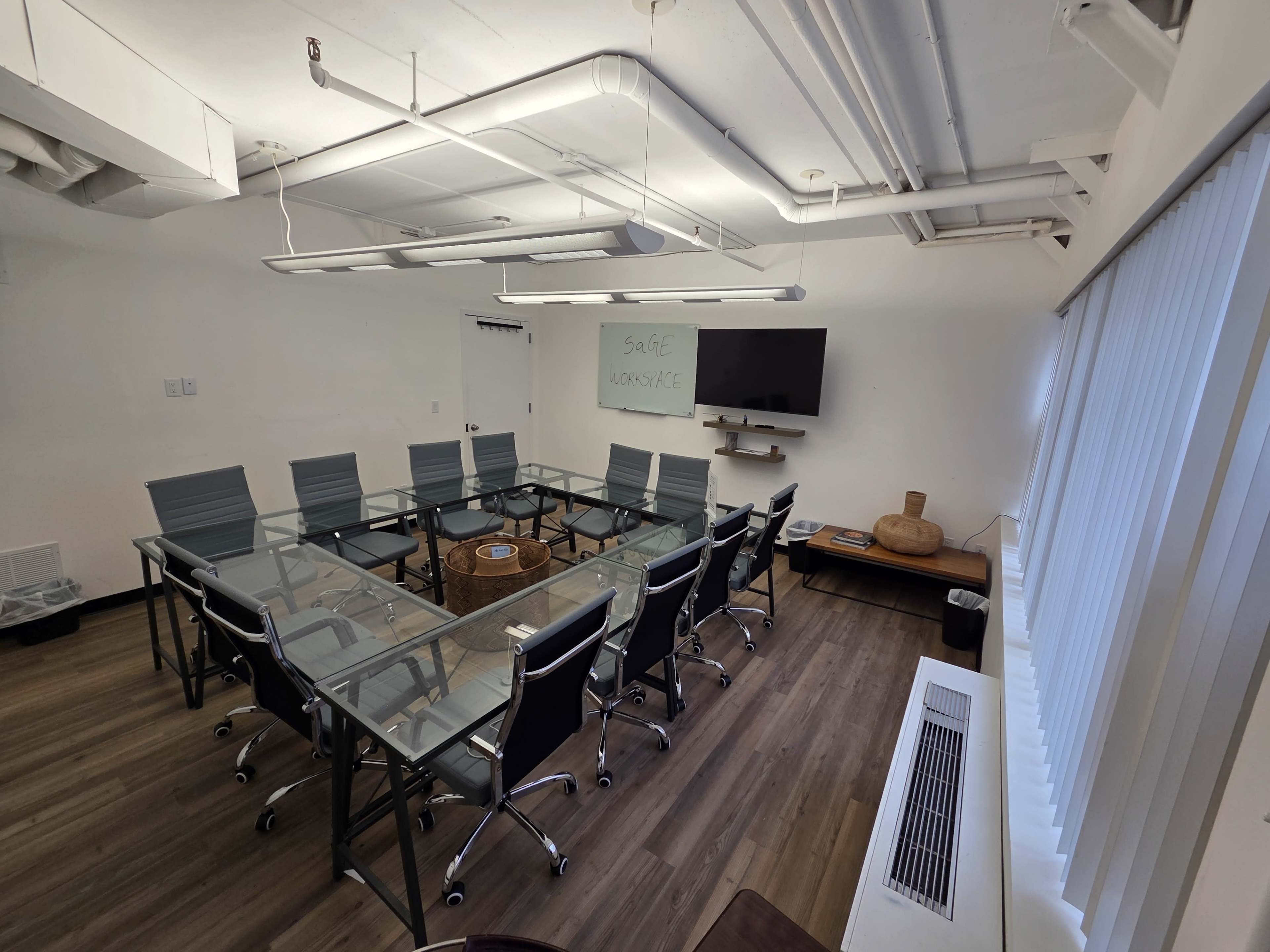 The image shows a modern conference room with a glass table, eight chairs, a wall-mounted TV, and a whiteboard with writing.
