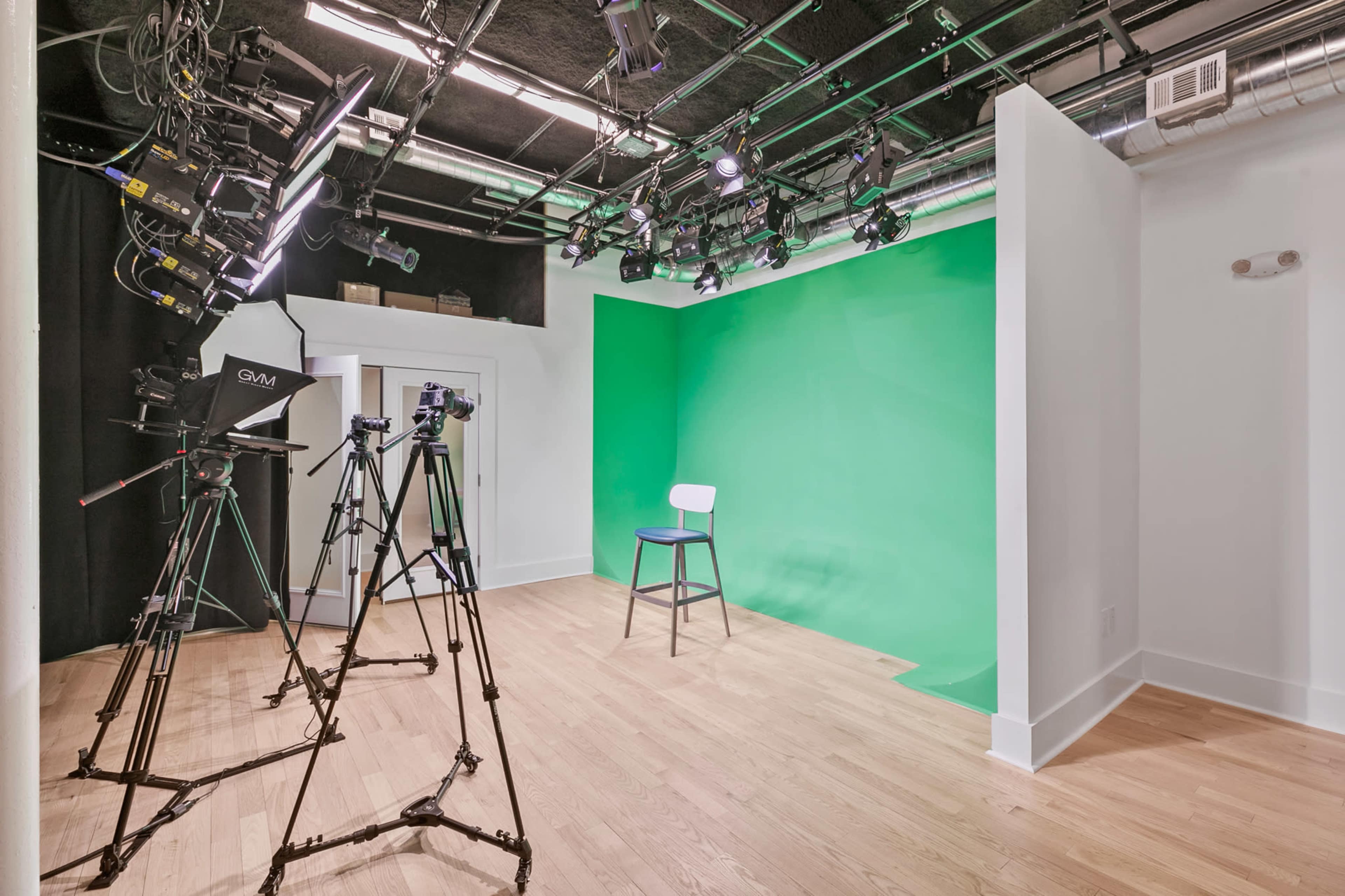 A studio with a green screen backdrop, a chair, and three cameras positioned on tripods.