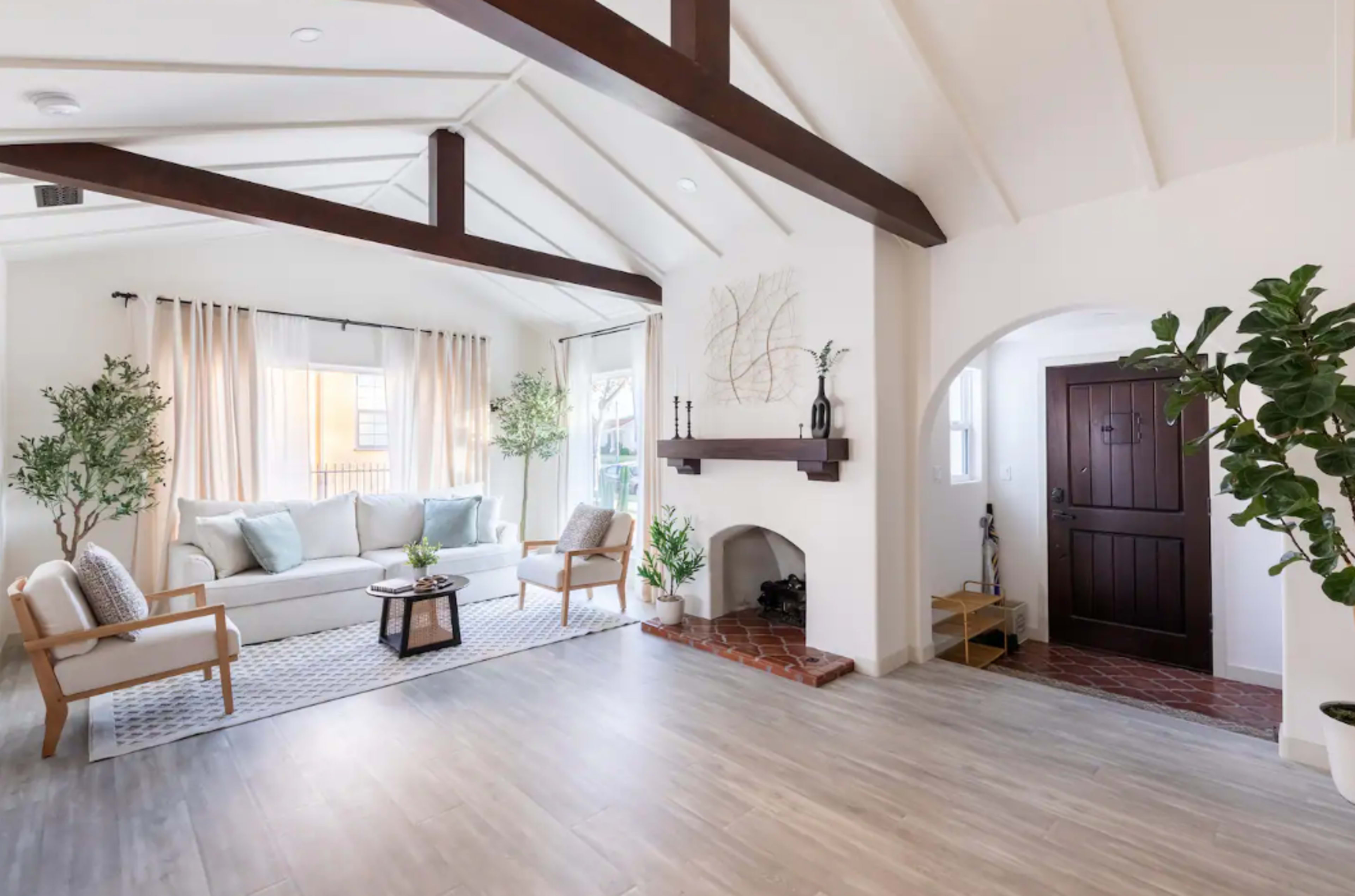 The room features a light-filled space with a seating area, a central coffee table, and a doorway leading to an entrance adorned with plants.
