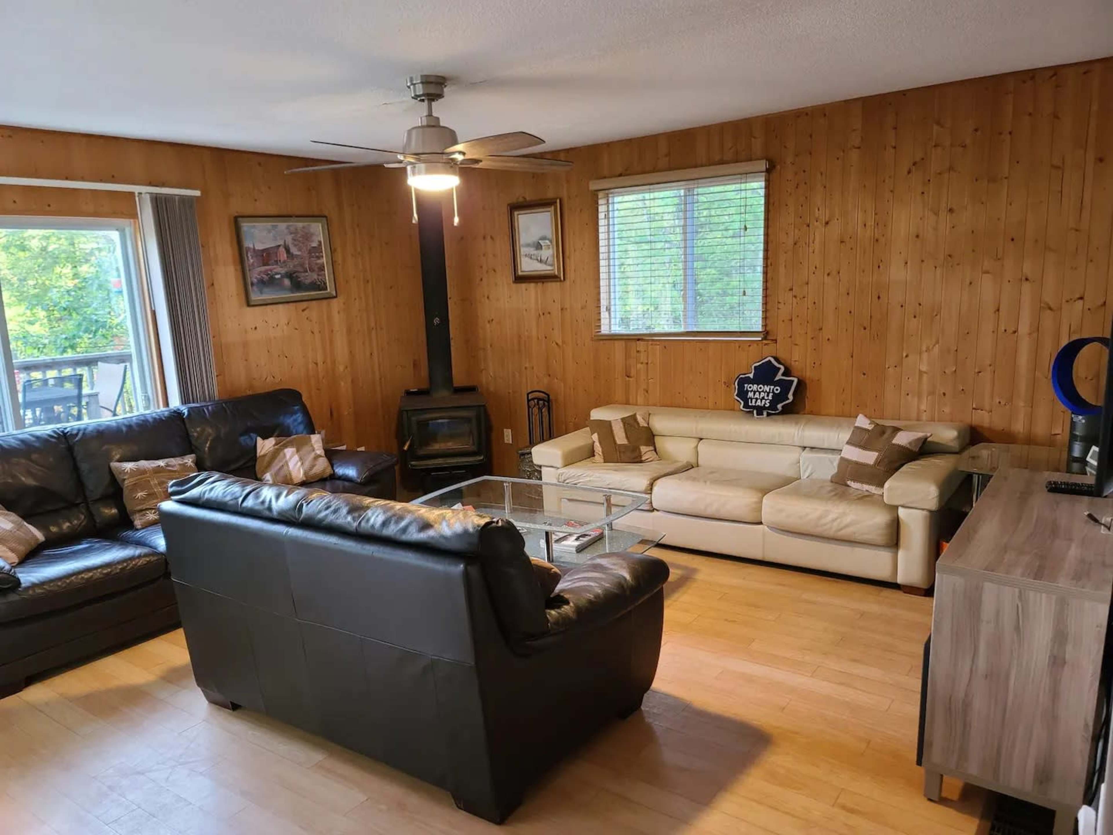 A living room with wooden paneling, two sofas, a glass coffee table, and a window letting in natural light.