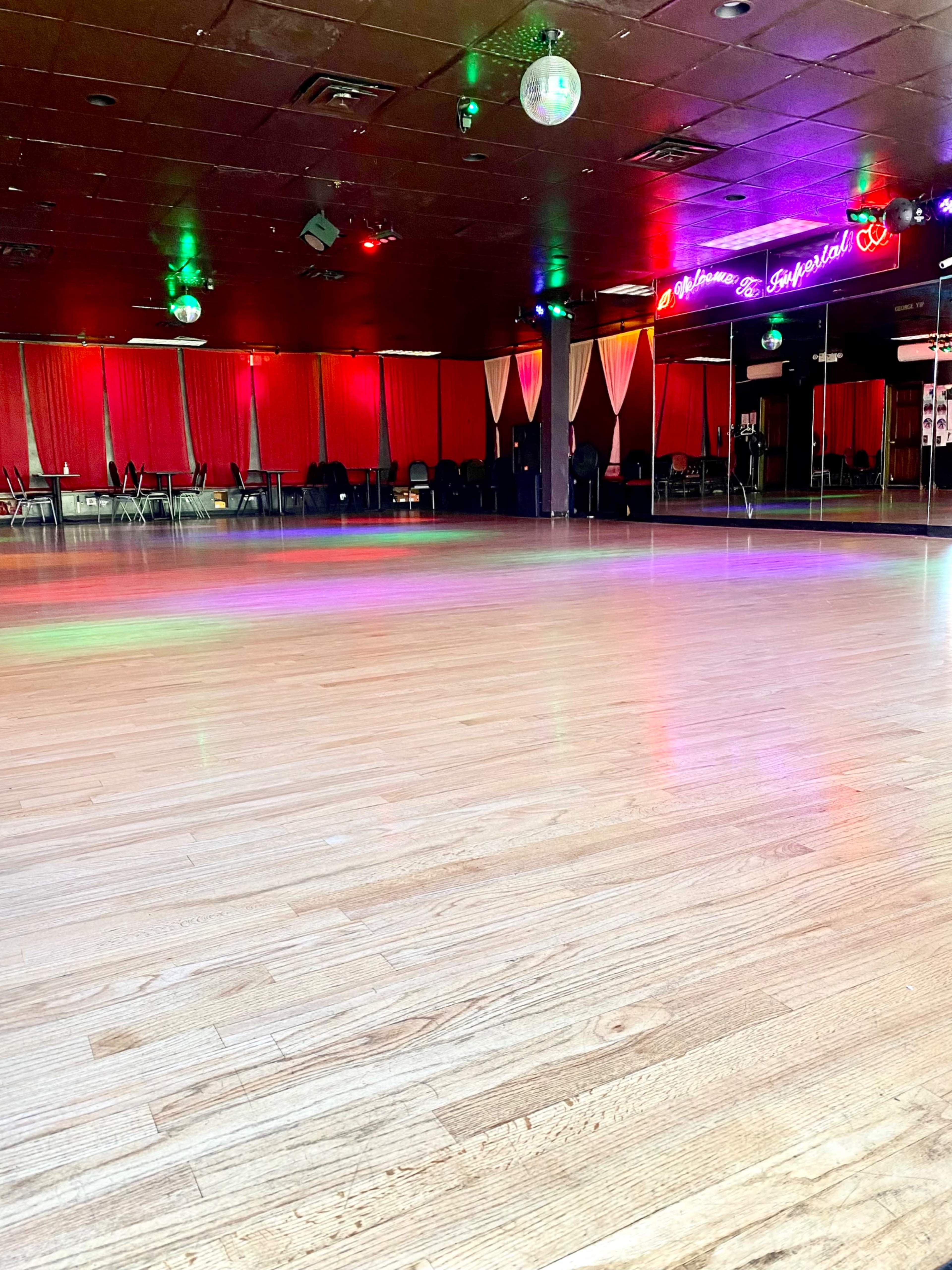 A spacious dance studio with a polished wooden floor and colorful lights reflecting off the walls.