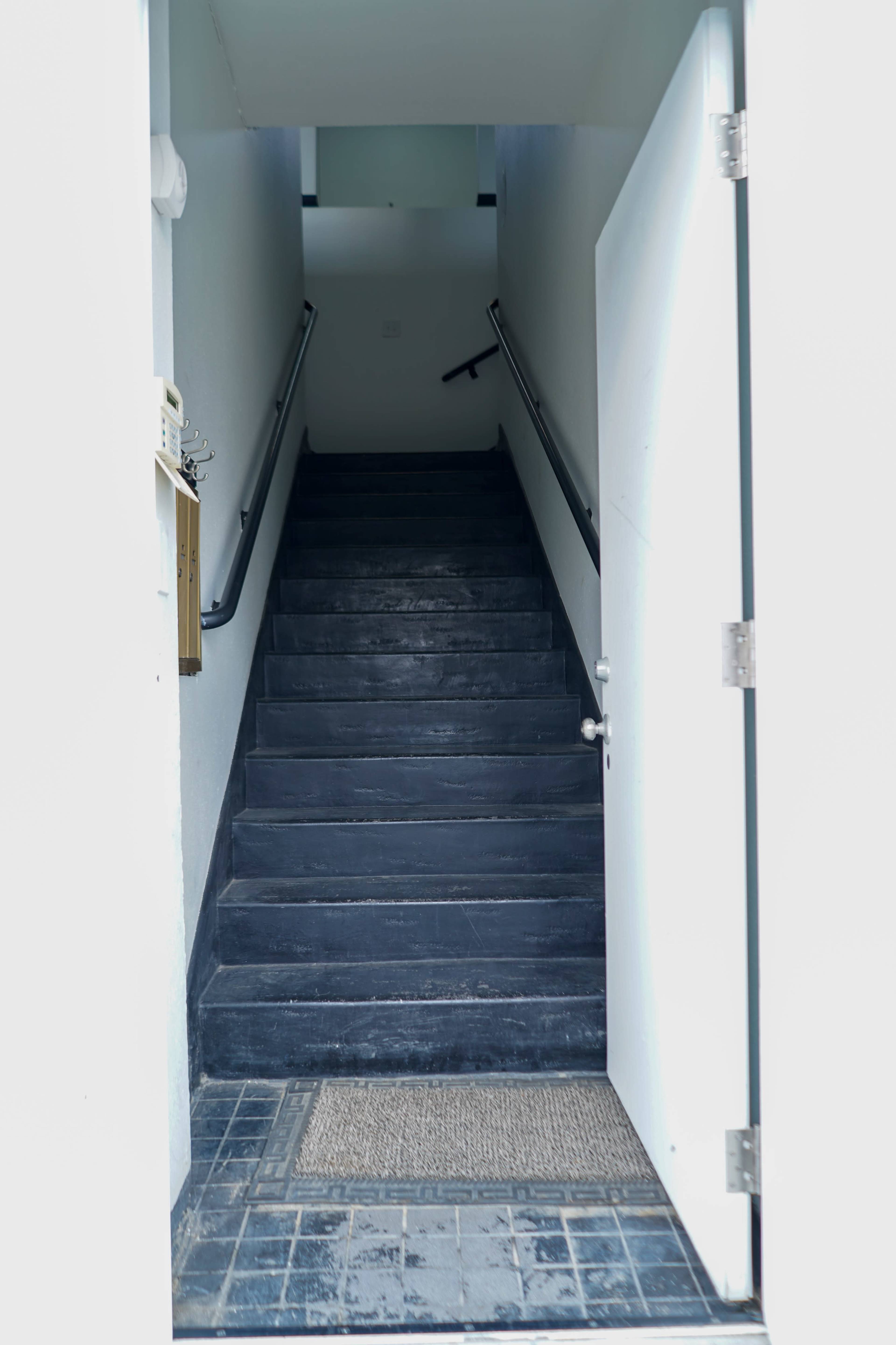 A staircase leads upward from an open door, with a rubber mat positioned at the entrance.