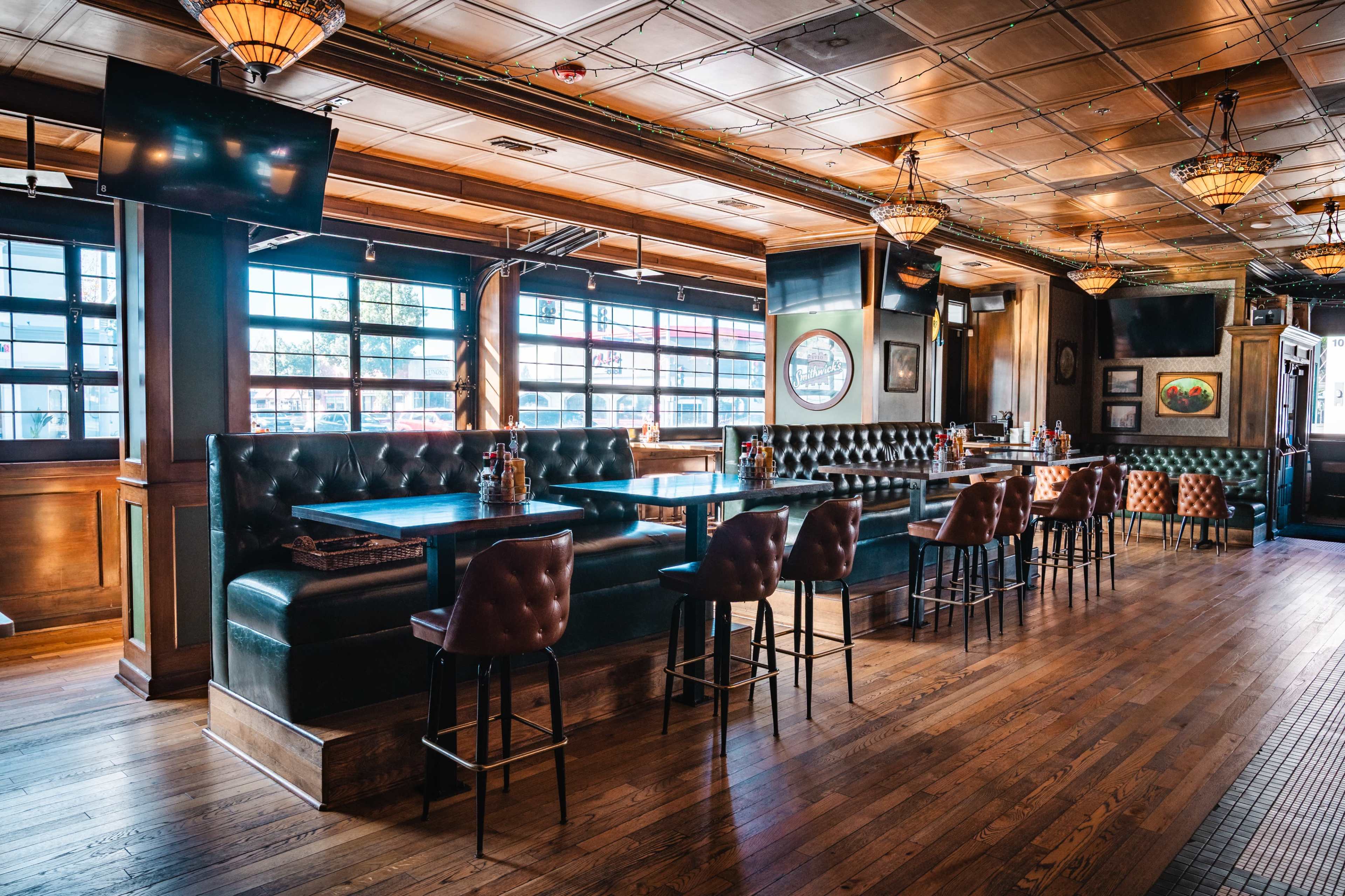 The image shows a spacious restaurant interior featuring dark wood floors, leather booth seating, and illuminated chandeliers.