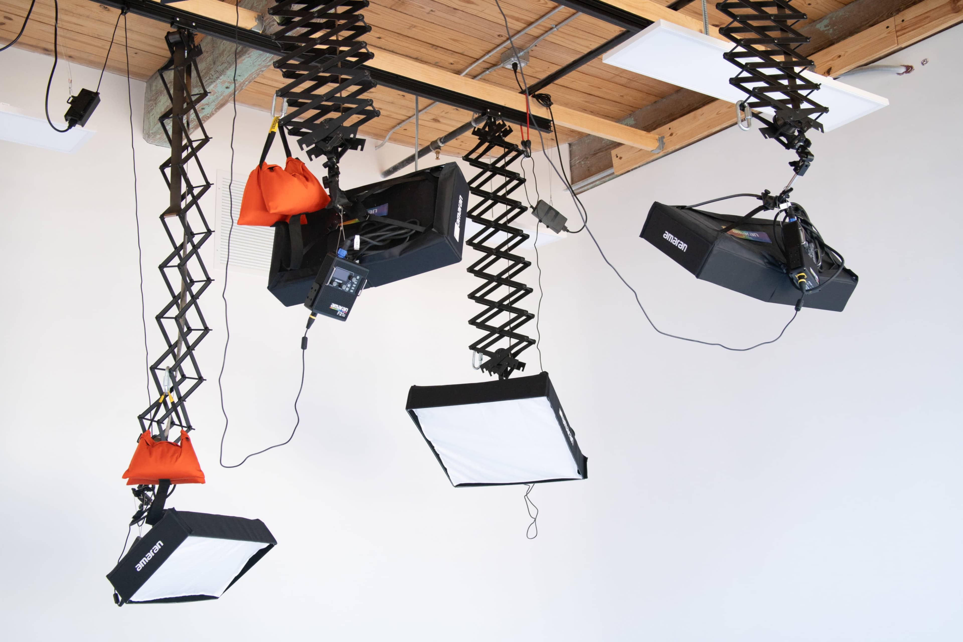 The image shows three studio lights suspended from the ceiling, with two of them having black boxes and one red weight for stabilization.