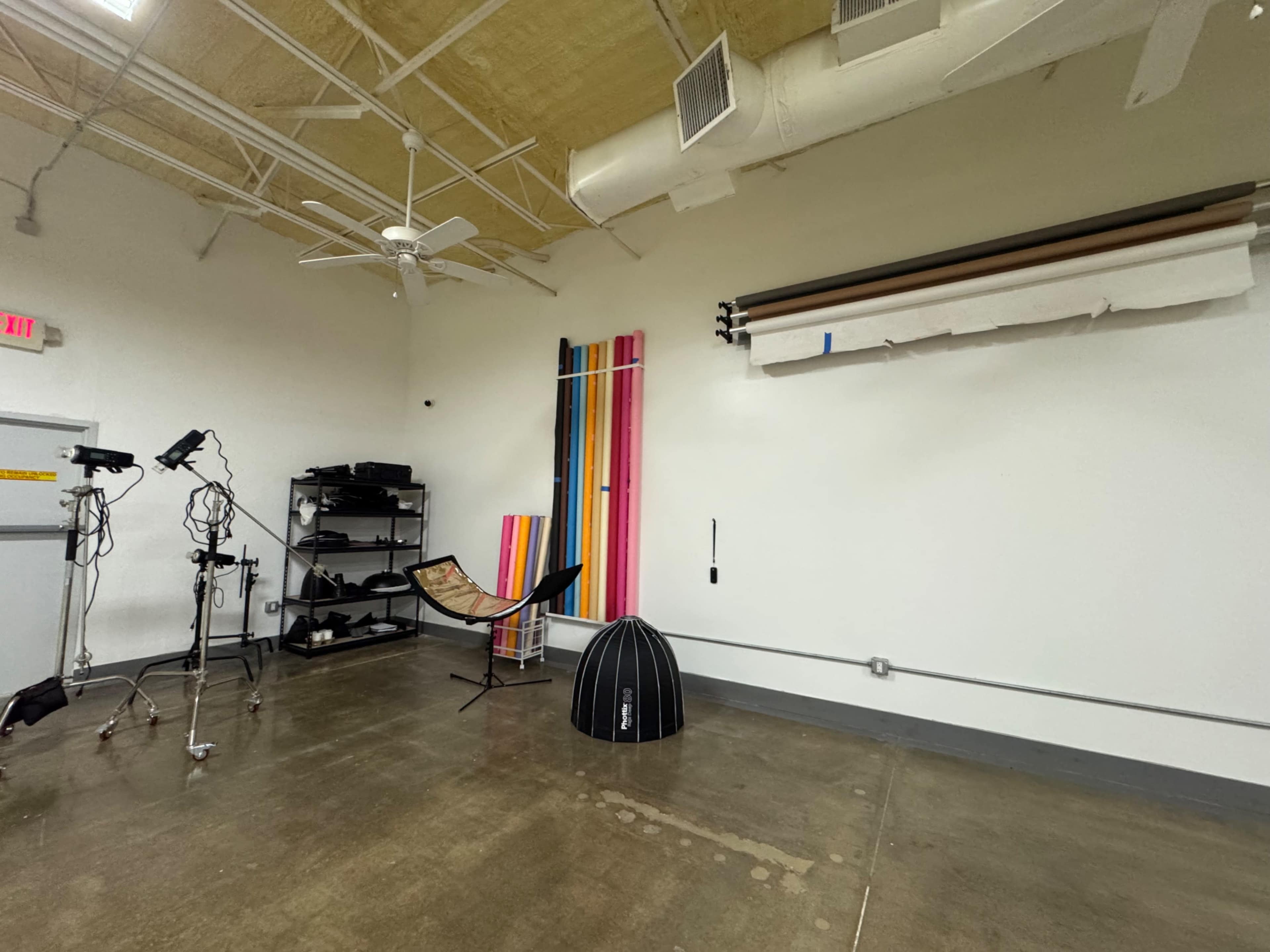 The image shows a photography studio with various backdrops, a hammock, lighting equipment, and a shelf for storing gear.