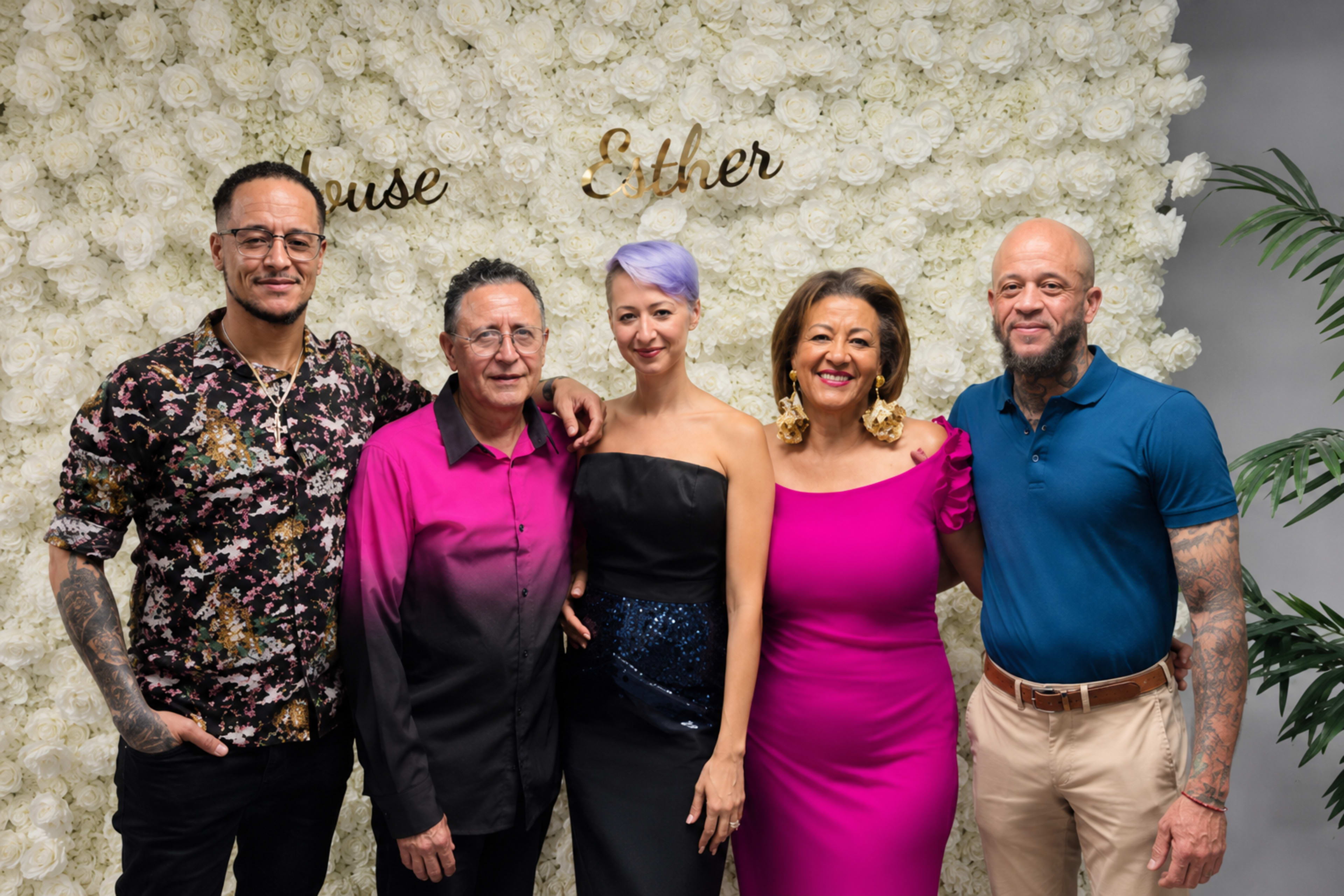 A group of five people poses together in front of a floral backdrop with the names "House" and "Esther" displayed.