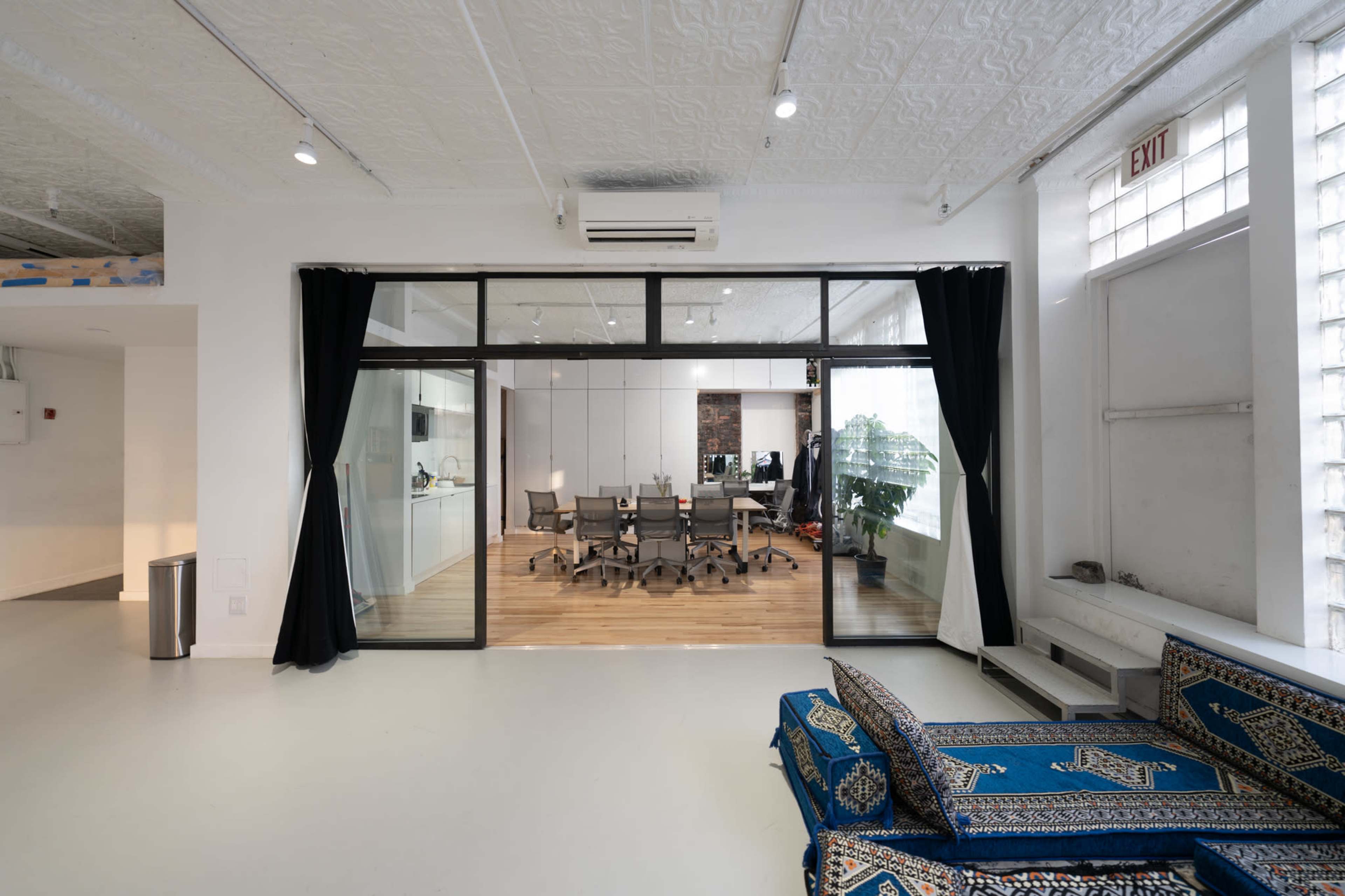 A modern office space with a glass wall separating a meeting area from a lounge area featuring a patterned couch.