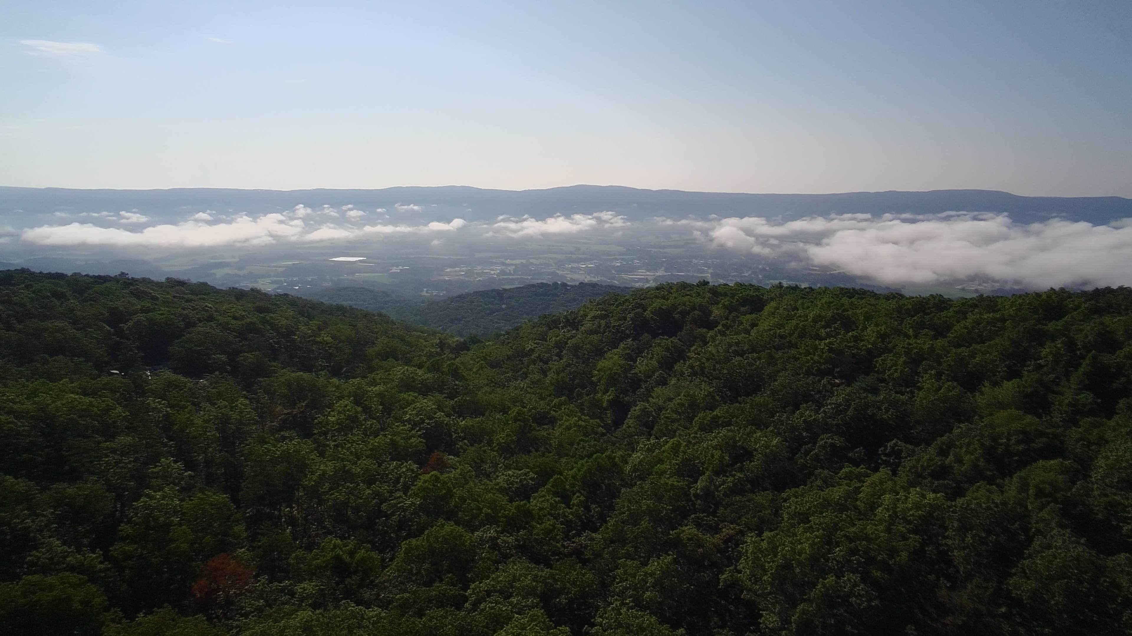 The scene shows a panoramic view of green hills and valleys with clouds hovering over the landscape in the distance.