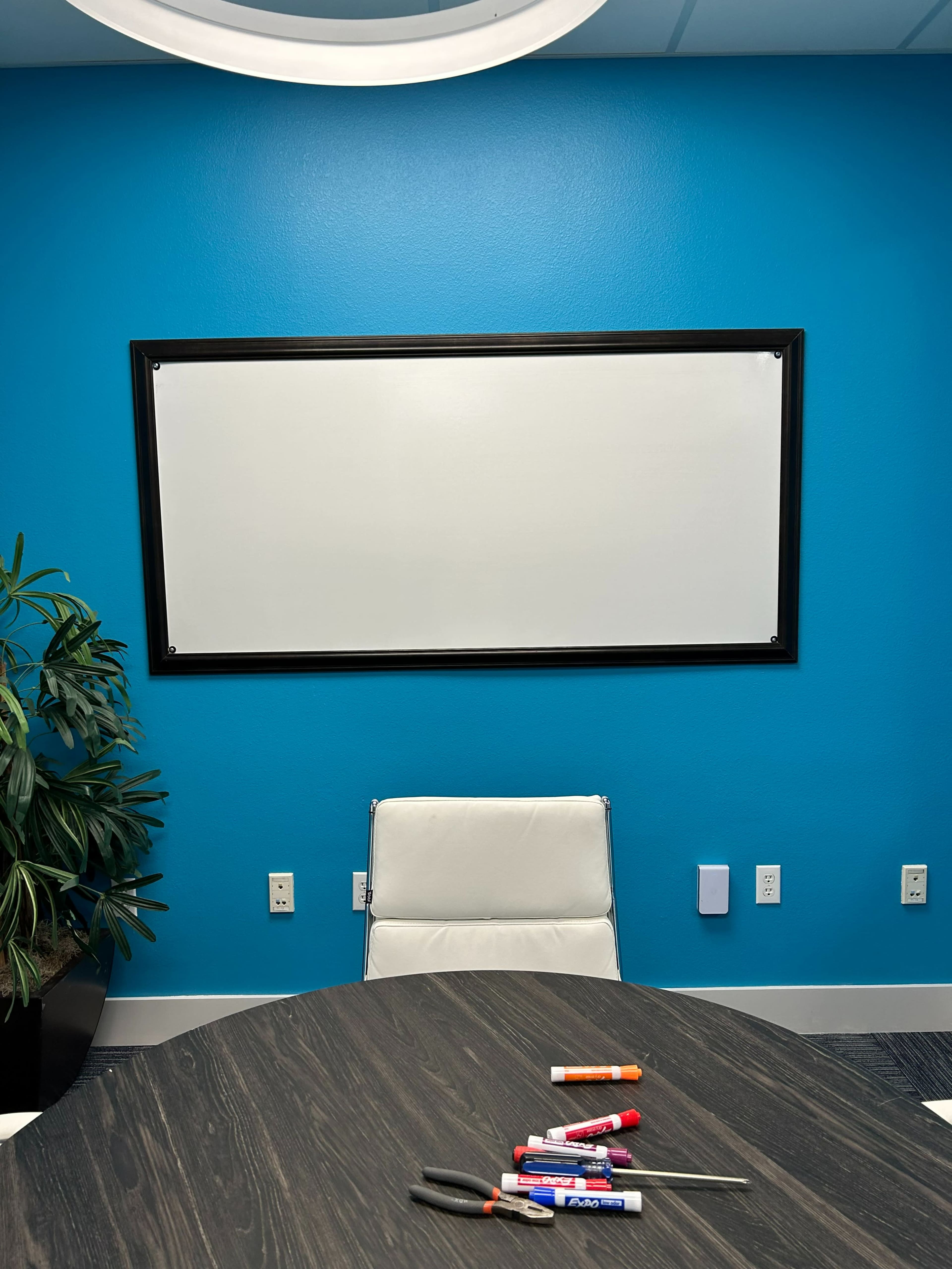 A modern conference room features a blue wall with a whiteboard, an empty chair, and office supplies on a round table.
