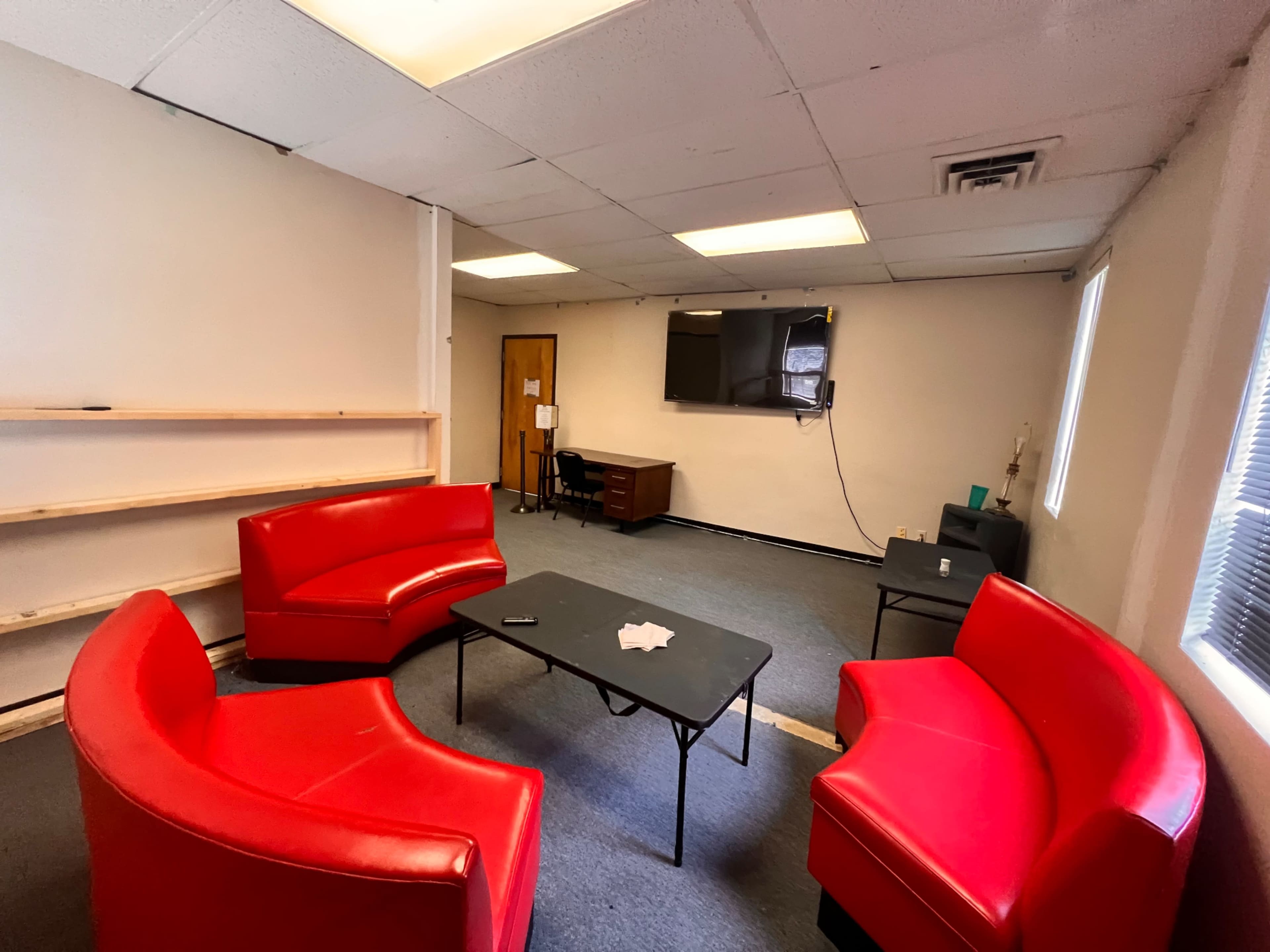A sparsely furnished room with two red curved sofas, a black table in the center, and a desk with a television mounted on the wall.