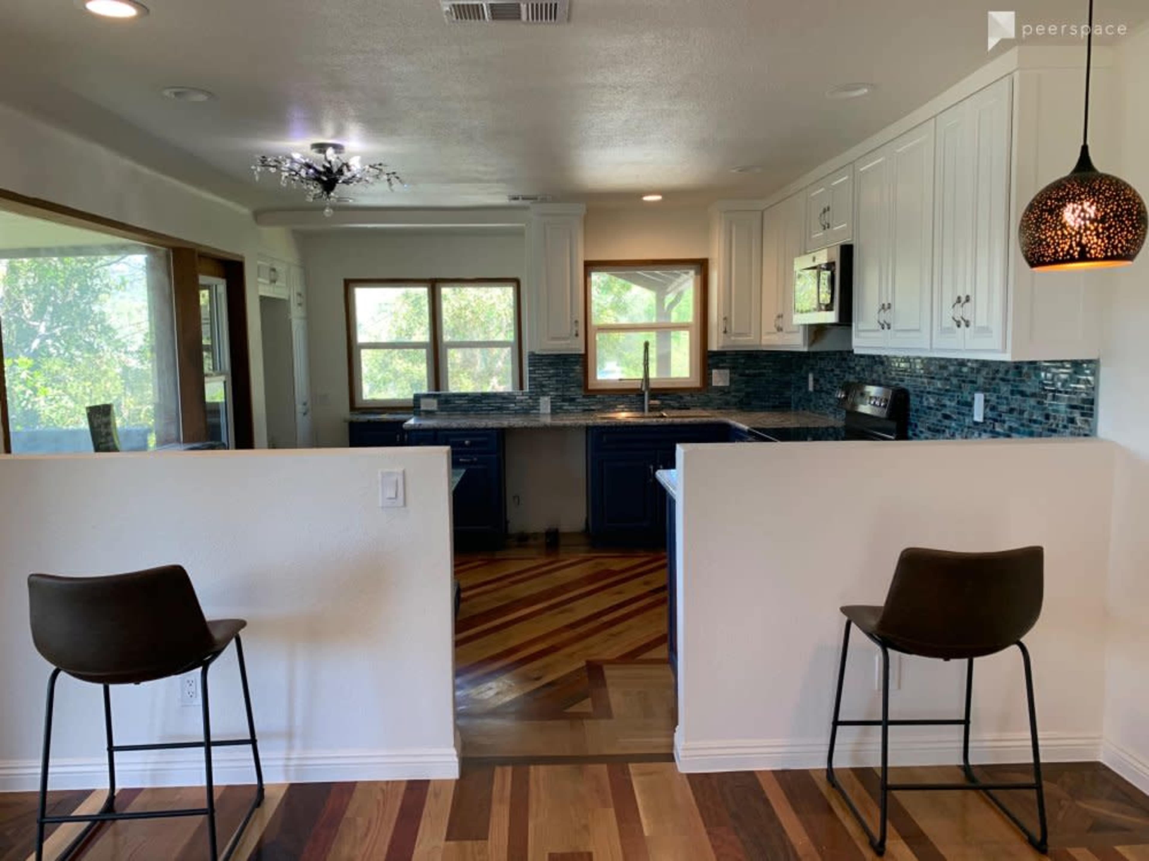 The image shows a modern kitchen with wooden floors, dark blue cabinetry, and two bar stools positioned at the counter.