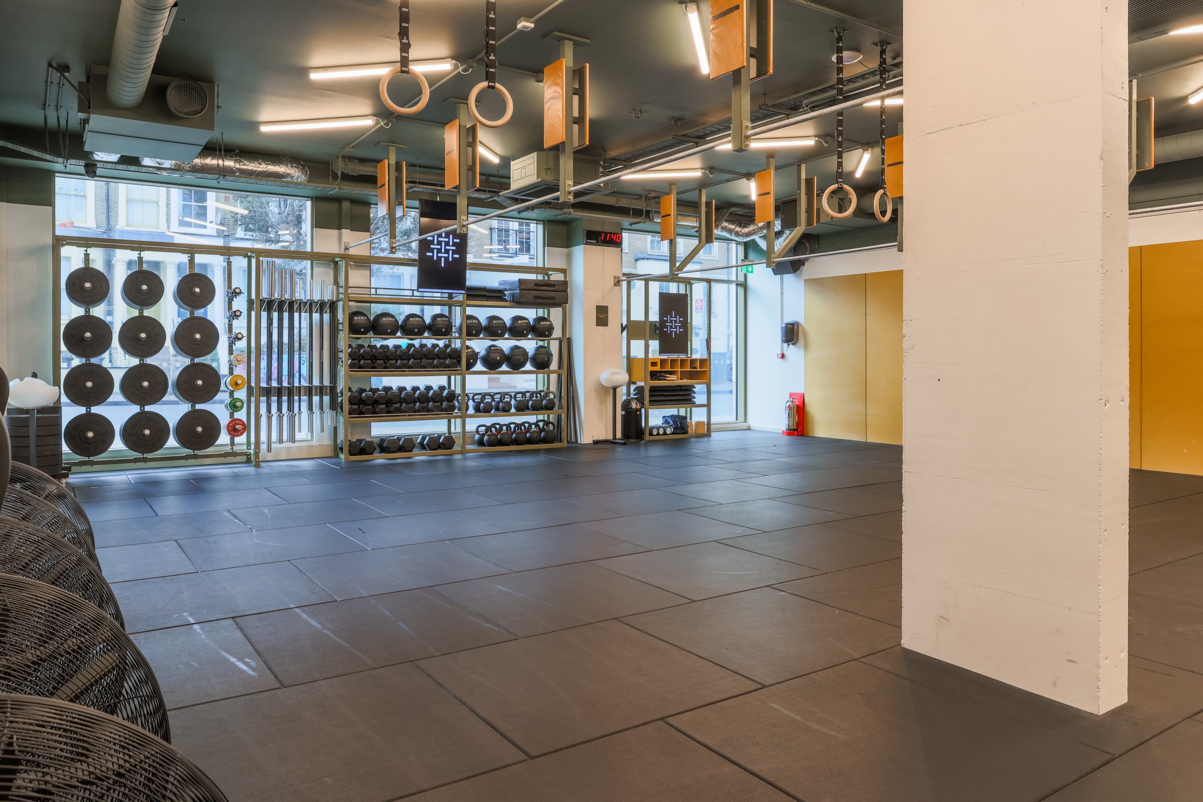 A fitness studio equipped with various gym weights, resistance bands, and gymnastic rings, with an open layout and large windows.