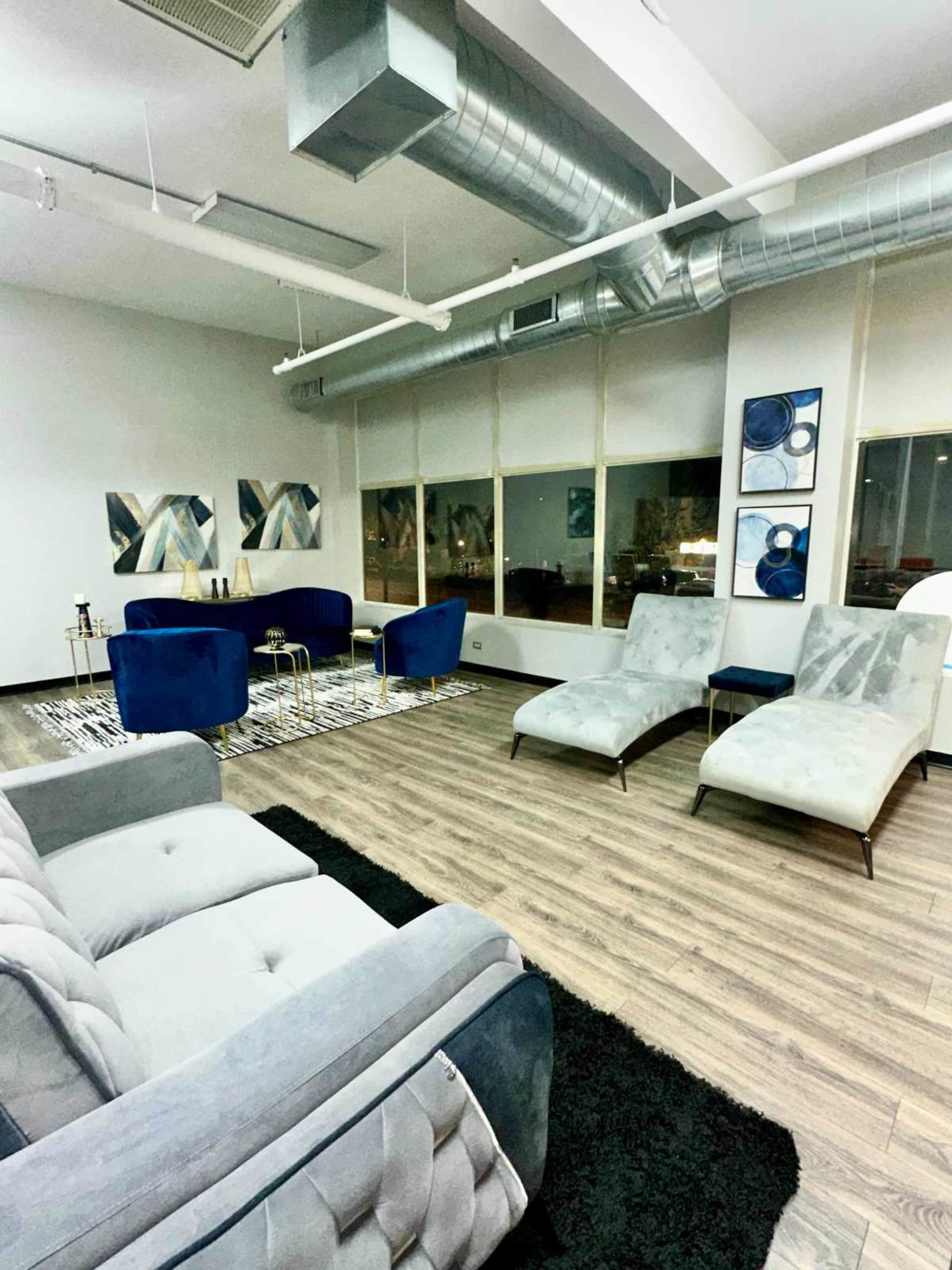 A modern lounge area with blue armchairs, chaise lounges, and abstract artwork on the walls overlooking a cityscape through large windows.