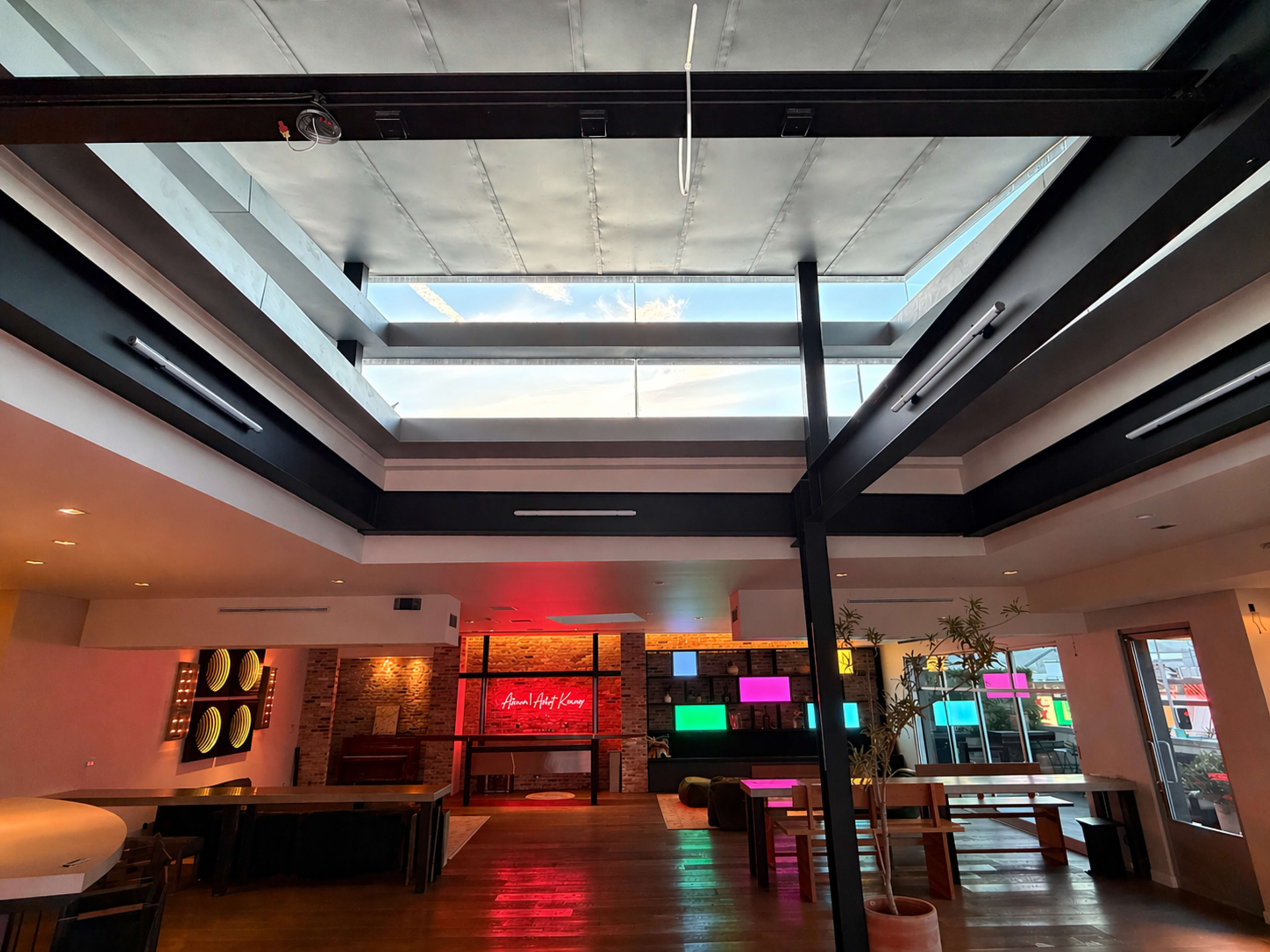 The image shows a contemporary interior space featuring large windows, modern furniture, and vibrant lights with a mix of open areas and separated sections.