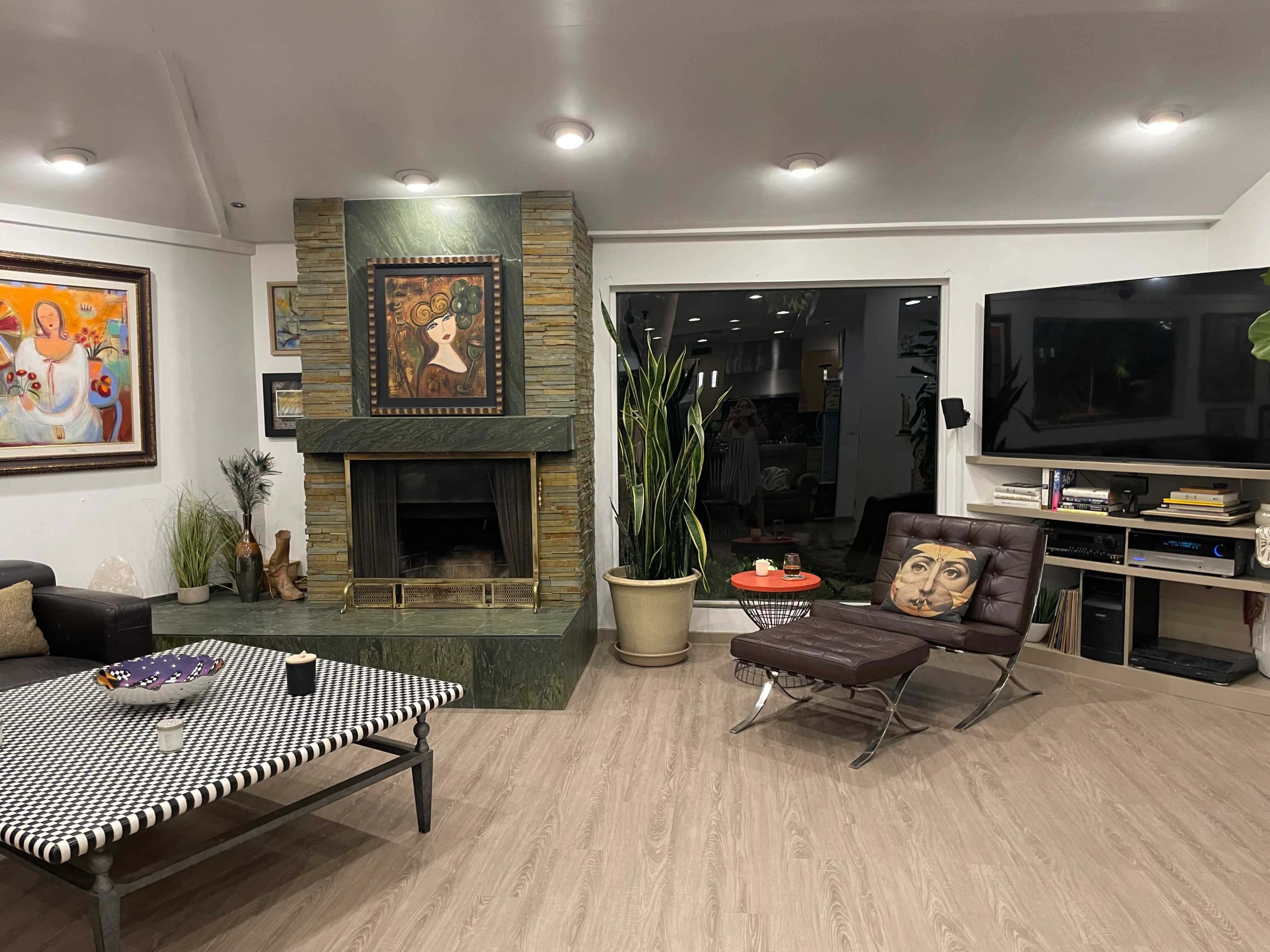 A modern living room with a stone fireplace, a black leather chair, and artwork on the walls.