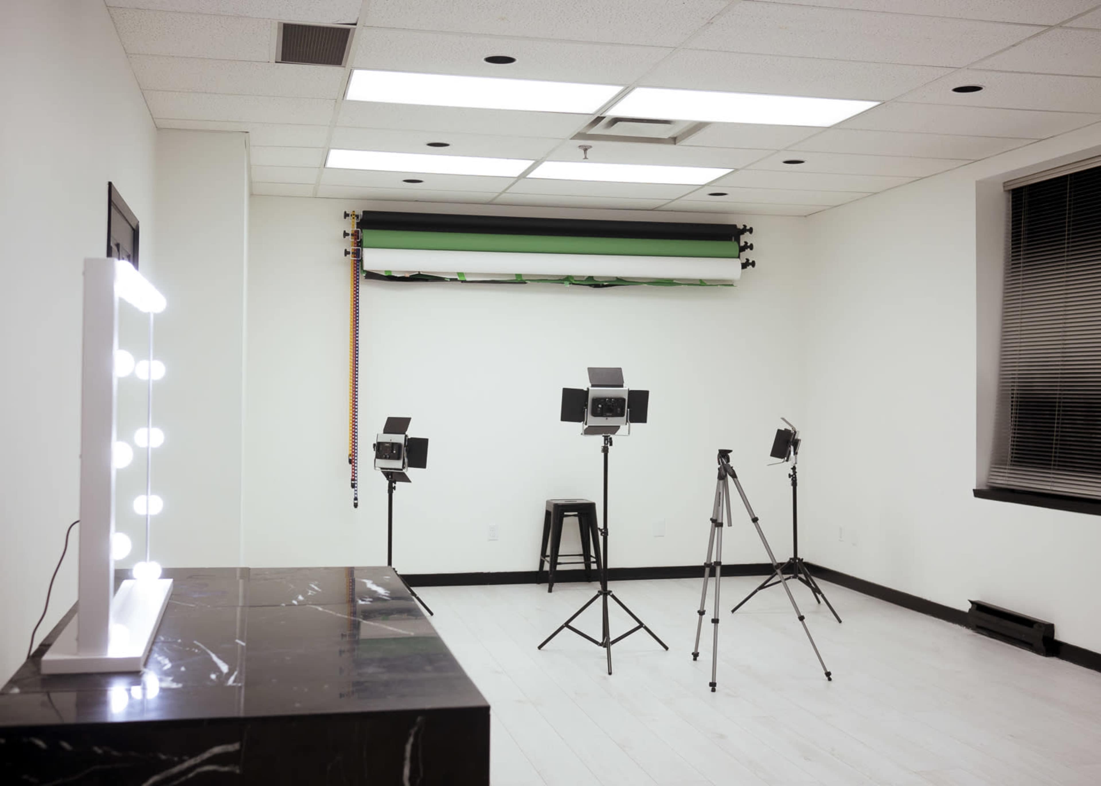 A well-lit studio space features three tripods with lights and a large mirror vanity against a white wall.
