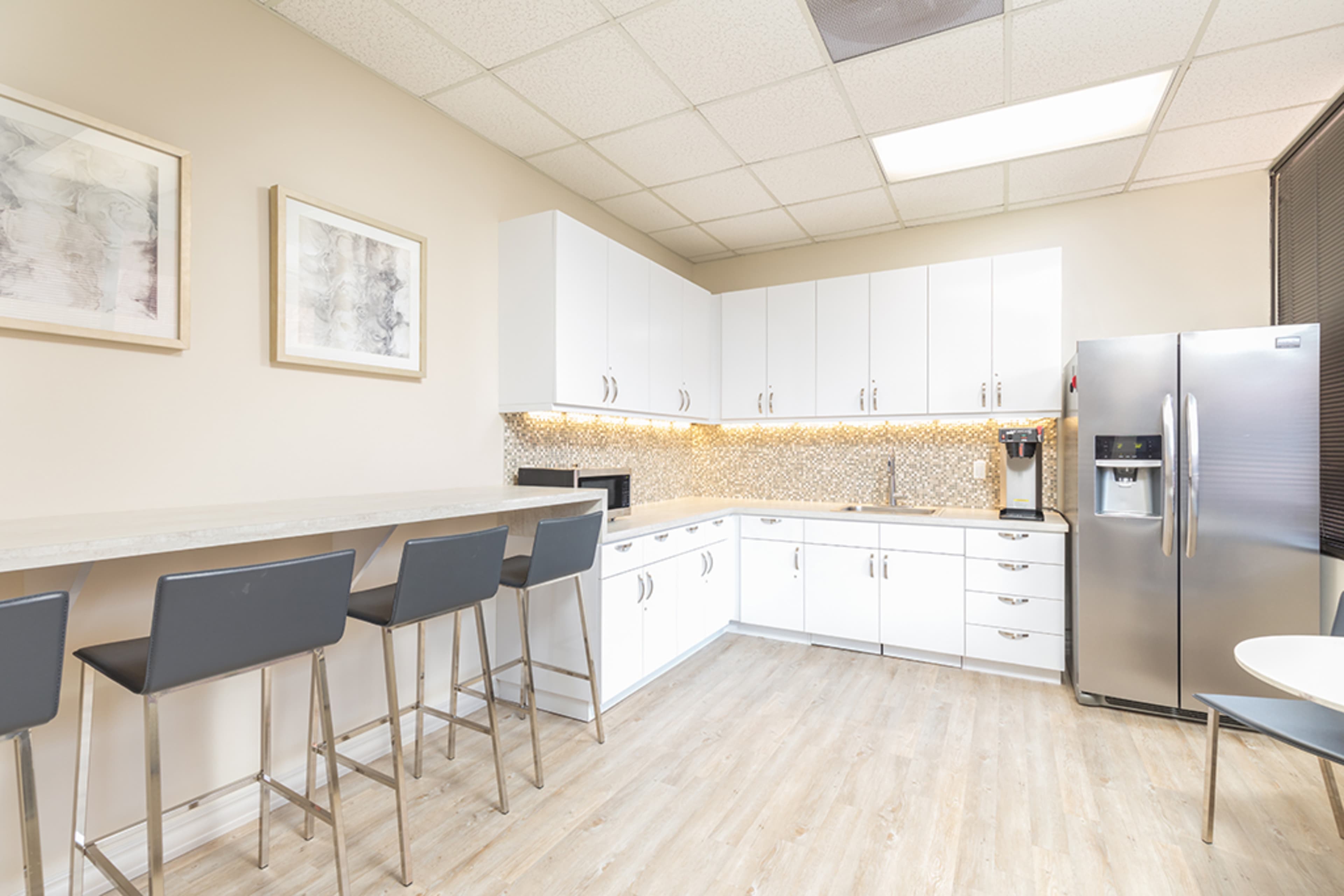 The image shows a modern kitchen with white cabinets, a countertop, a refrigerator, and barstool seating along one side.
