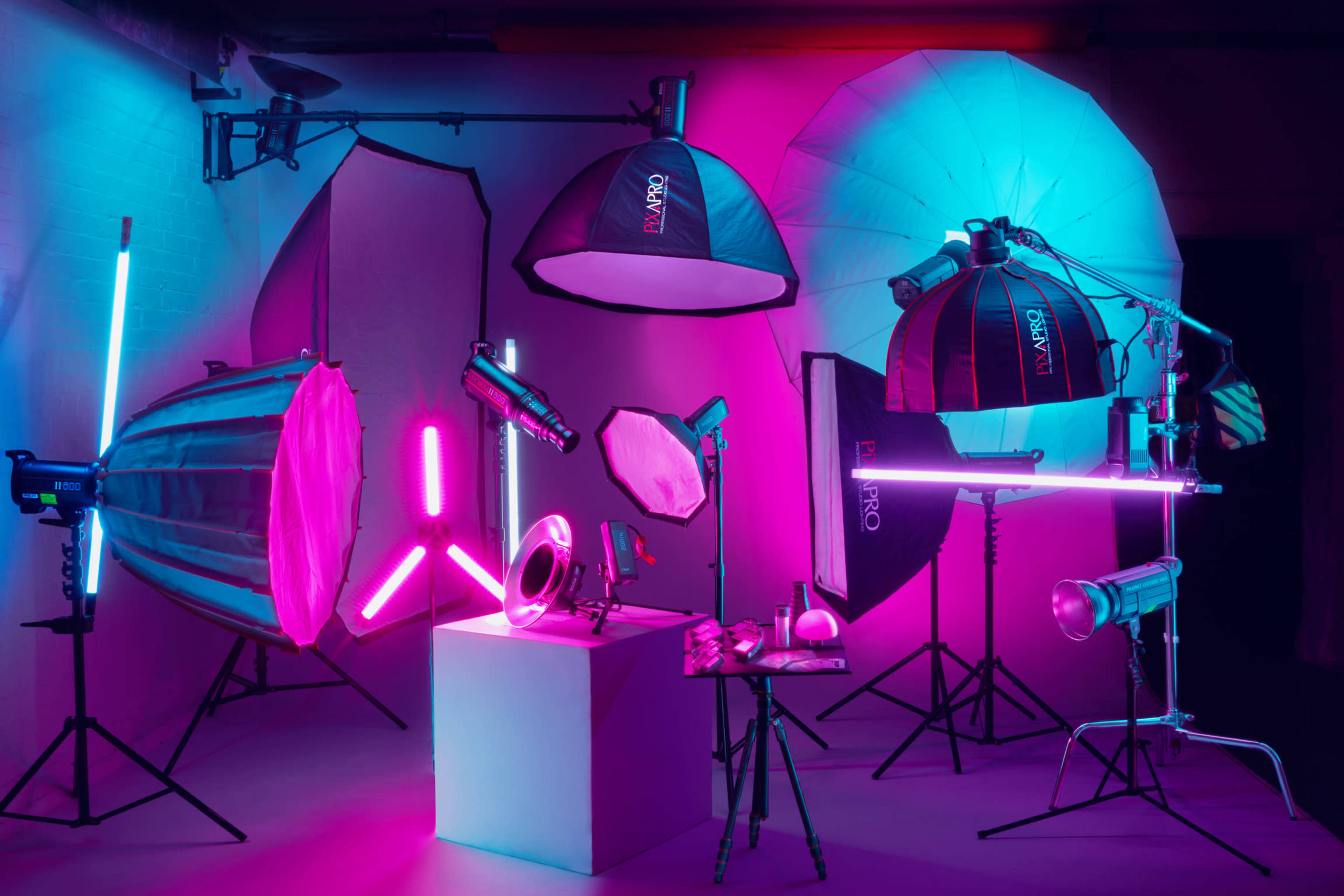 A variety of professional photography lighting equipment, arranged against a colorful backdrop with pink and blue lighting.