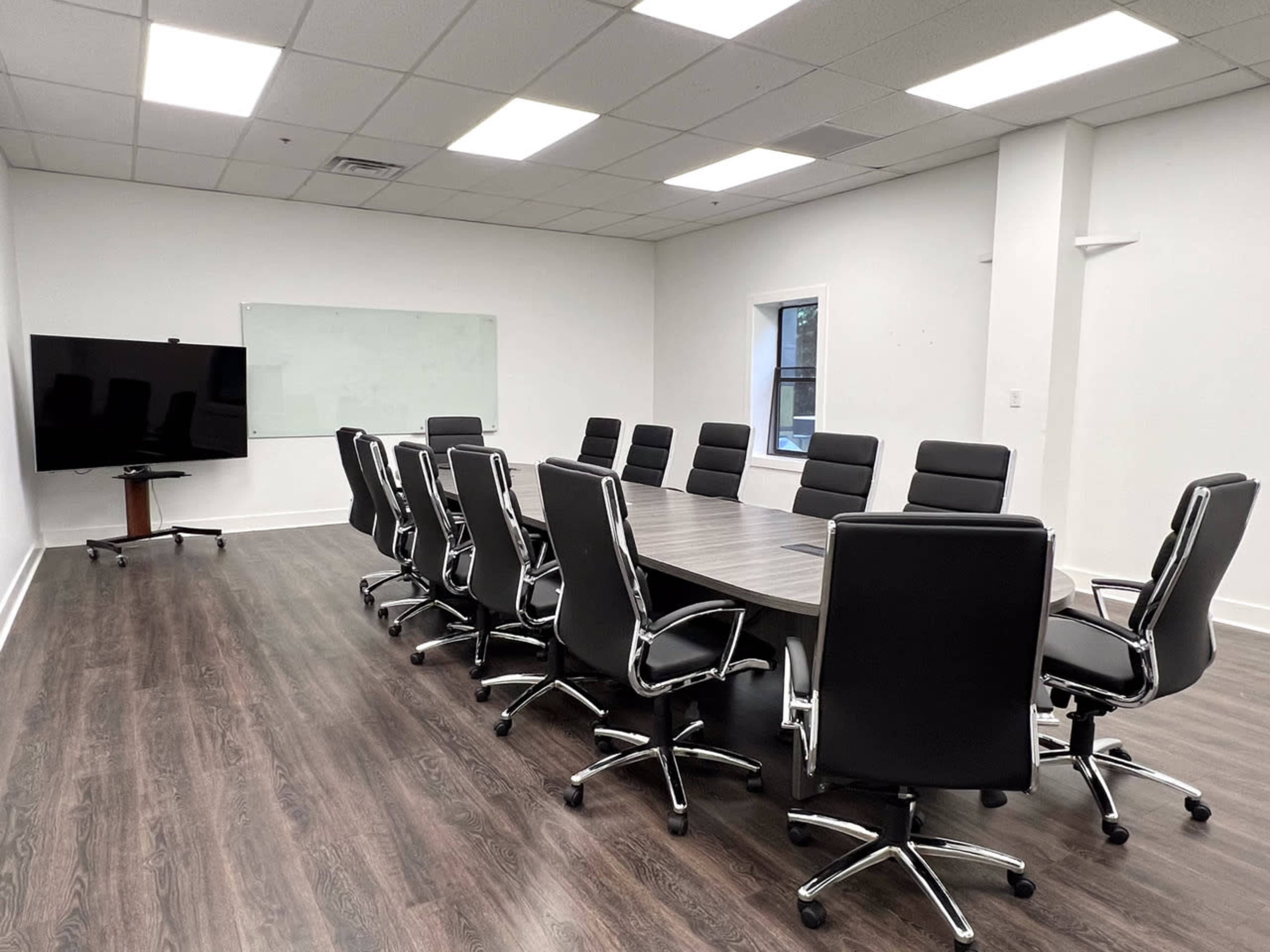 A large conference room features a long table surrounded by black office chairs, a television on a stand, and a whiteboard on the wall.