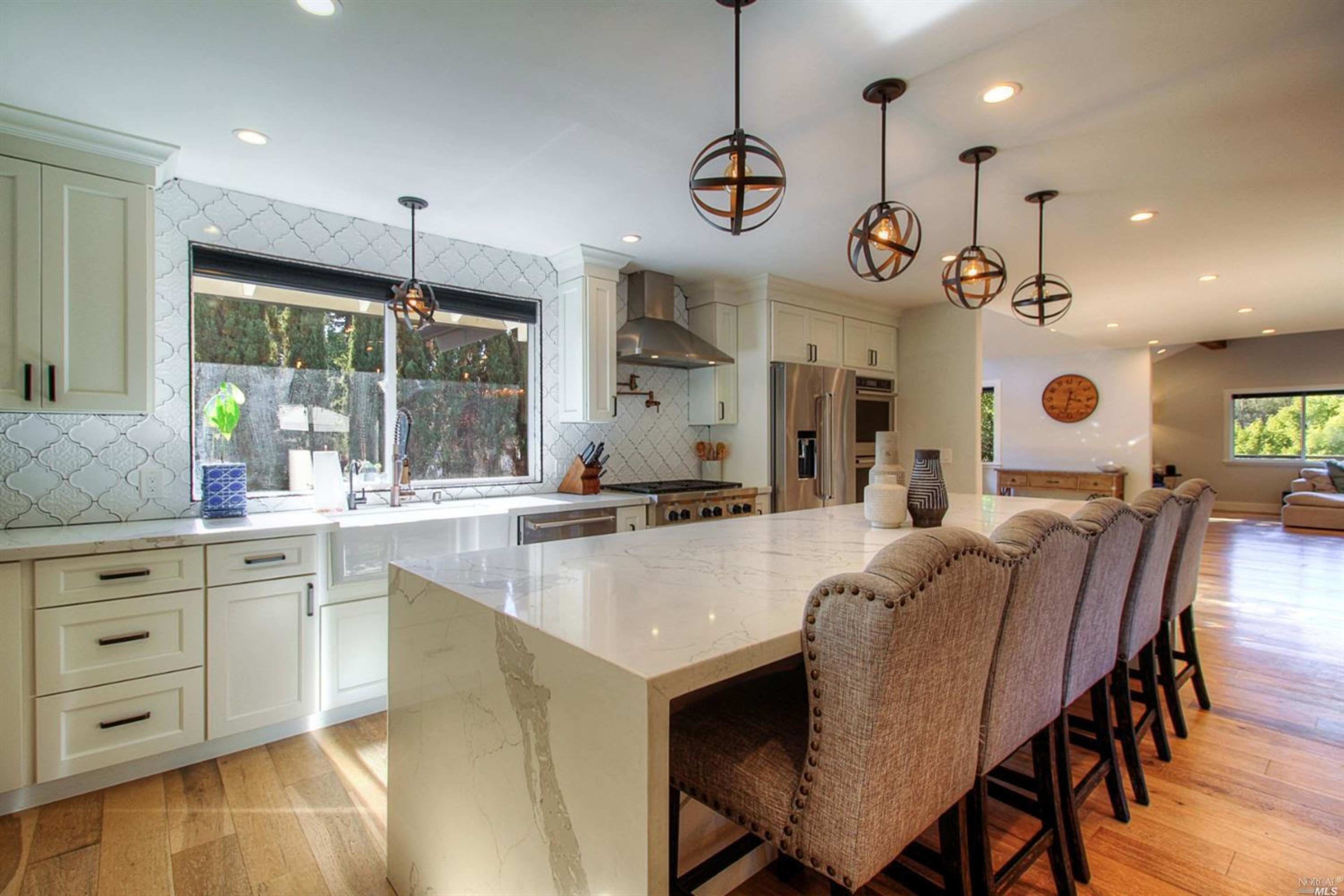 A modern kitchen features a large island with bar seating, pendant lights, and a spacious layout with stainless steel appliances.