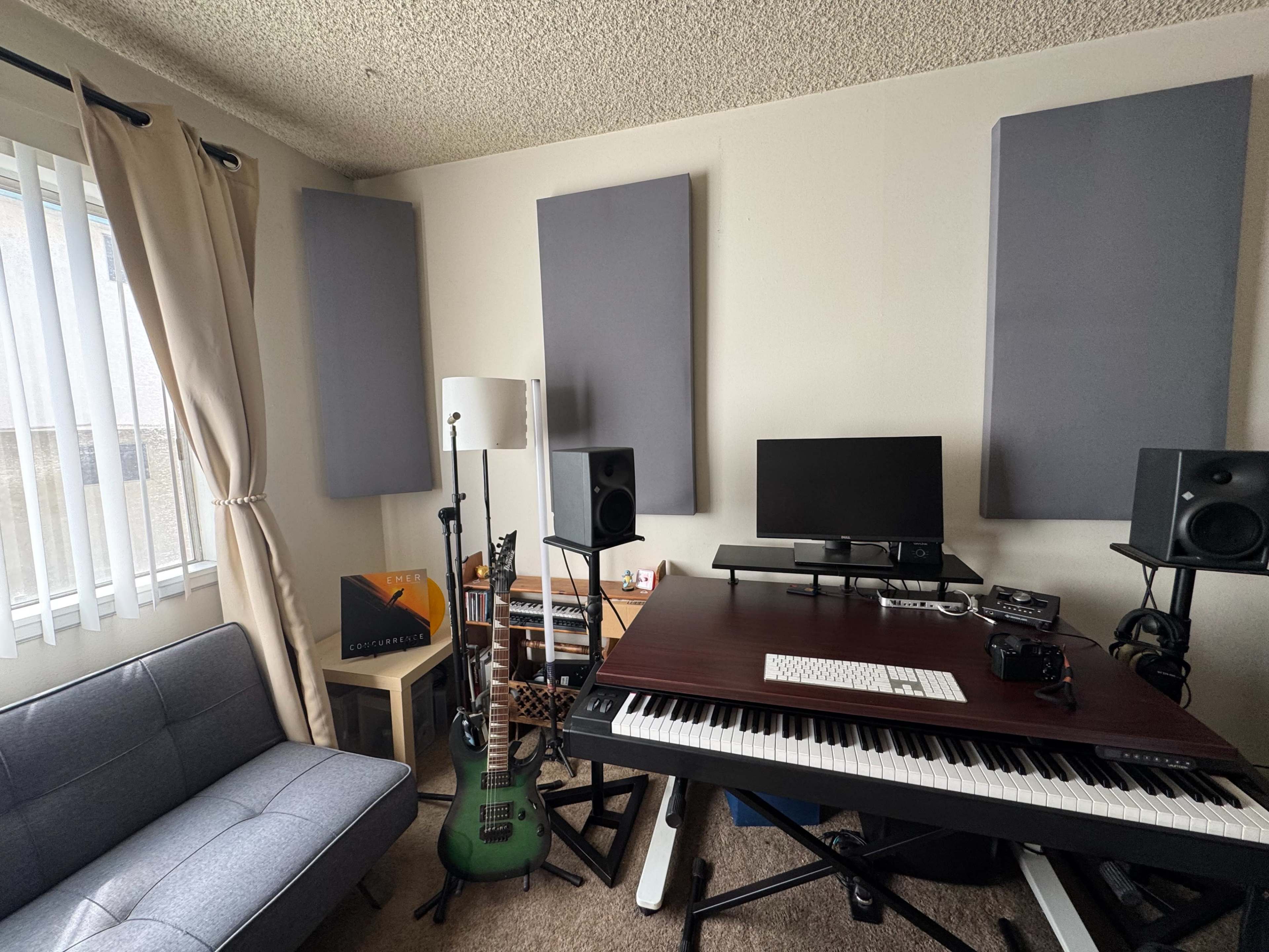 A small music studio is shown, featuring a keyboard, monitors, a guitar, and soundproofing panels on the walls.