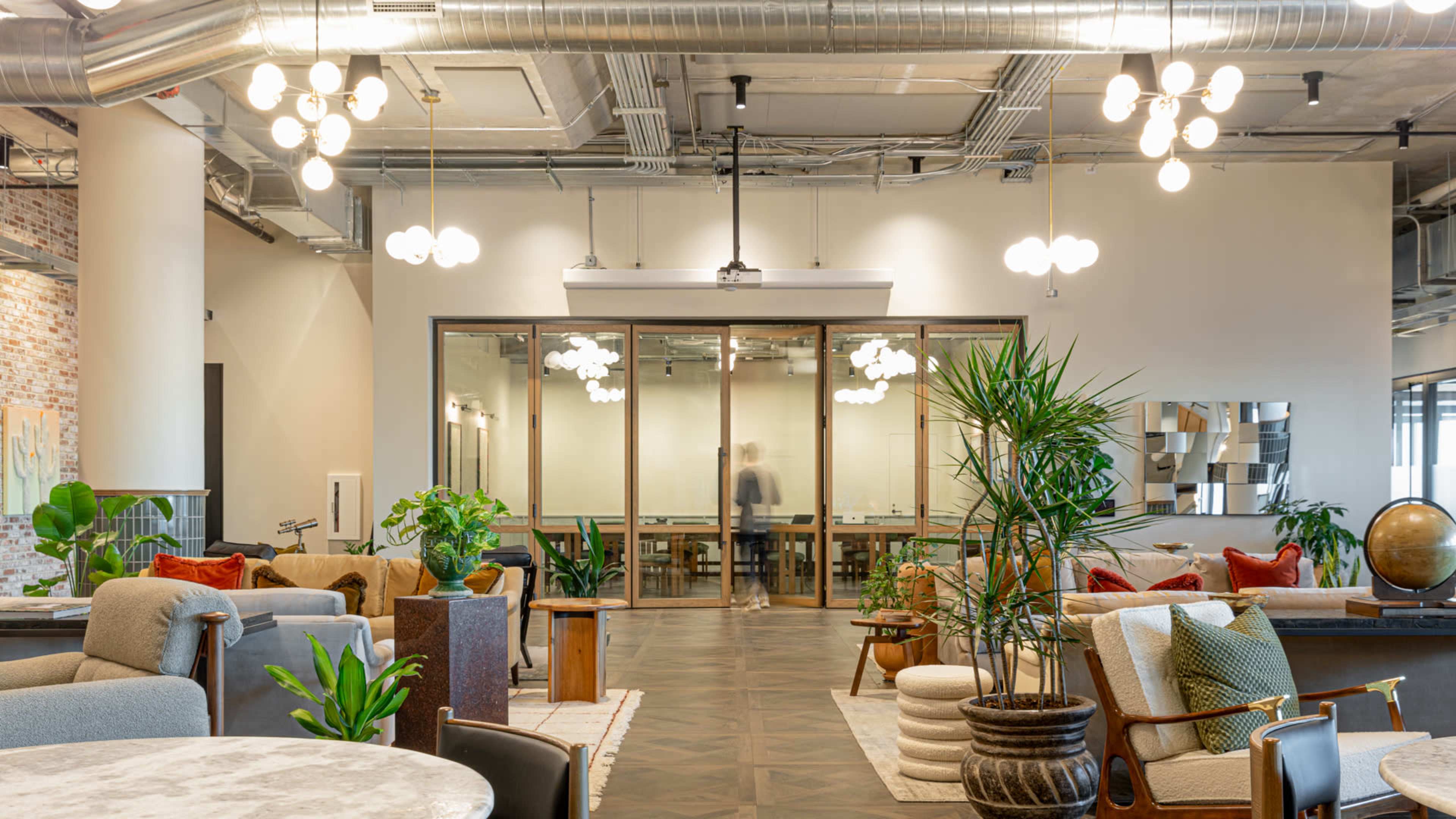 A modern office space featuring various seating areas, plants, and a conference room with glass walls.