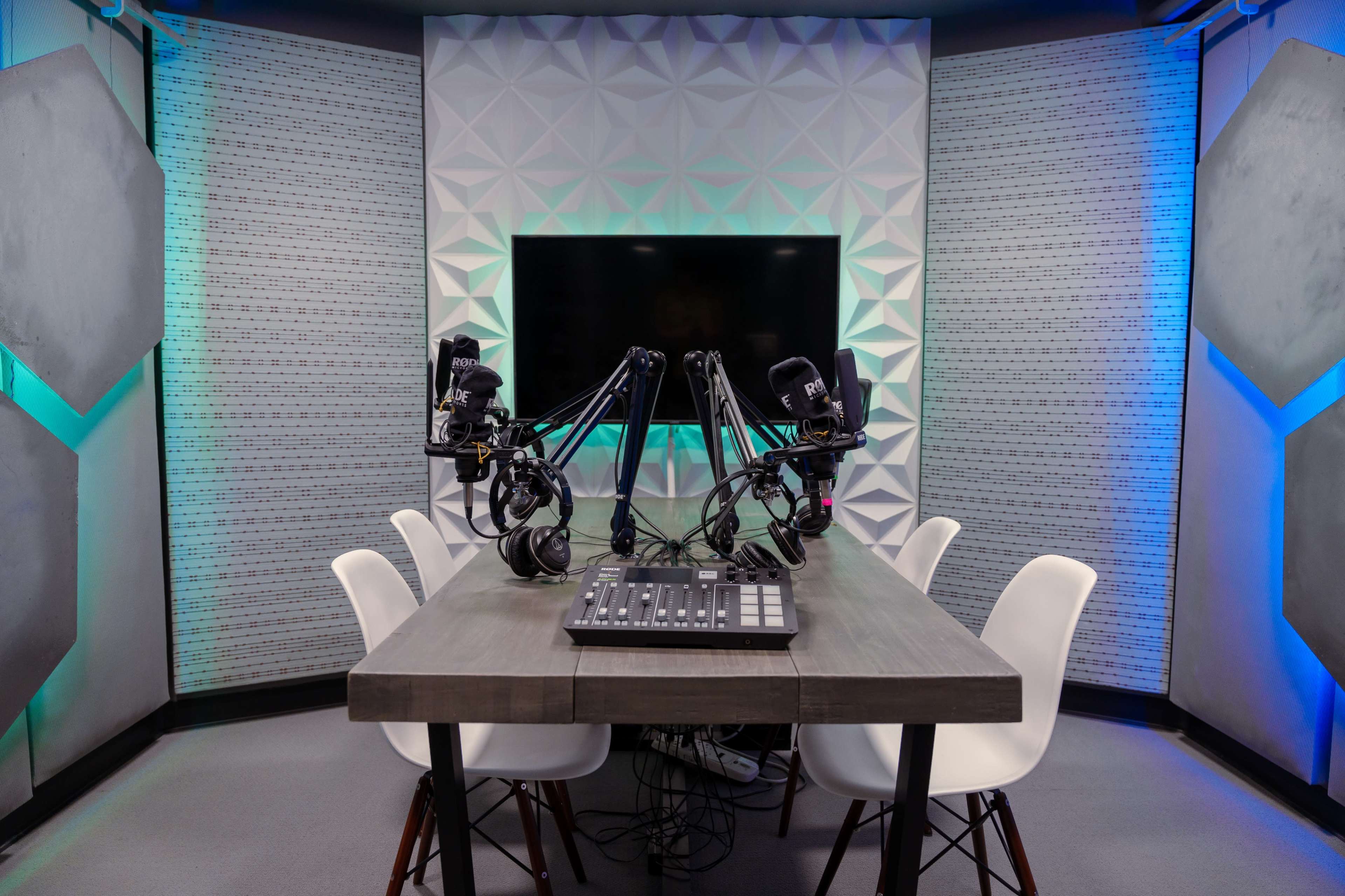A podcast recording studio equipped with a table, four chairs, and two mounted microphones.