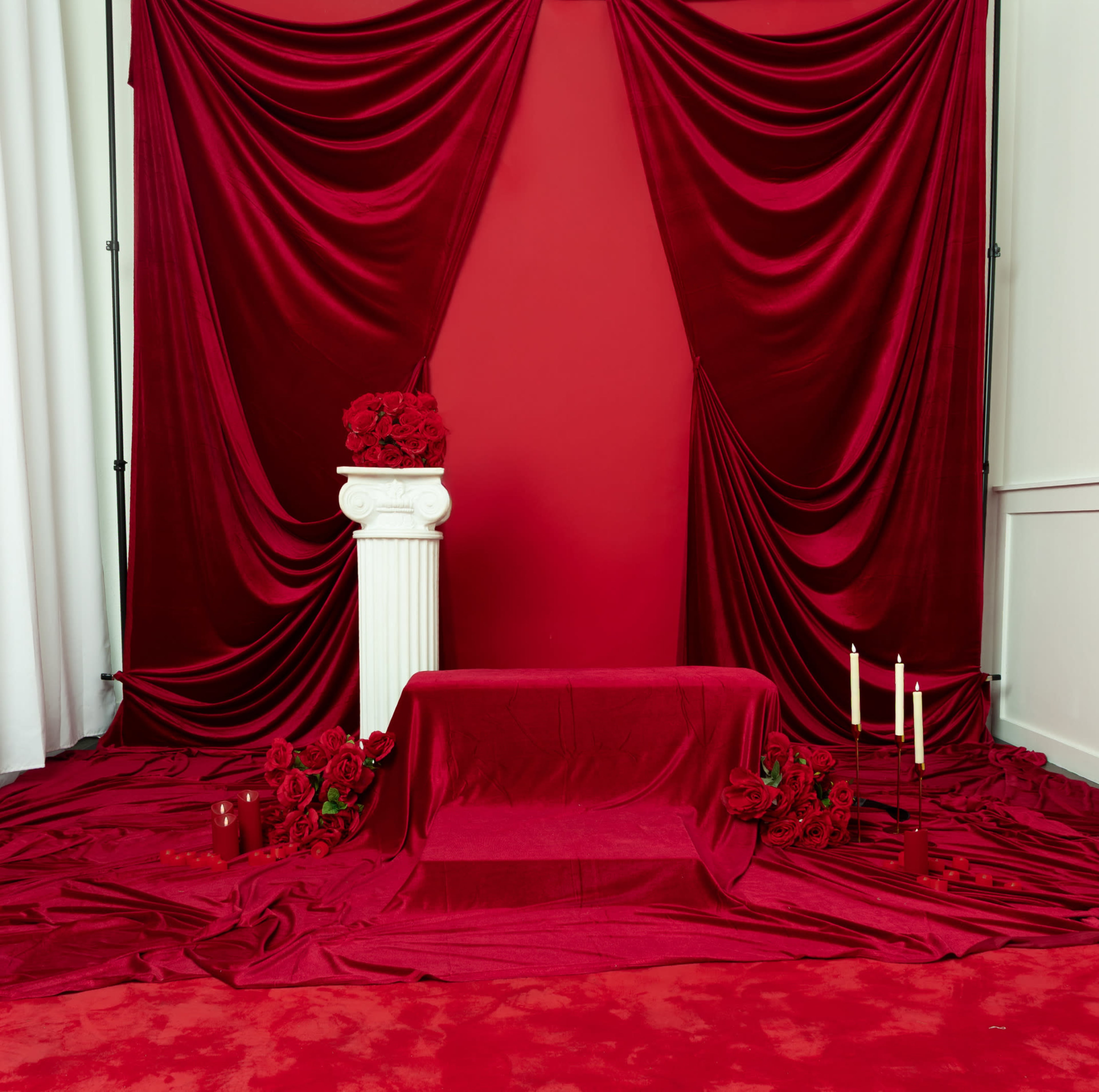 The scene features a red-themed backdrop with draped fabric, a white column, and candles arranged around a table, all surrounded by red roses.