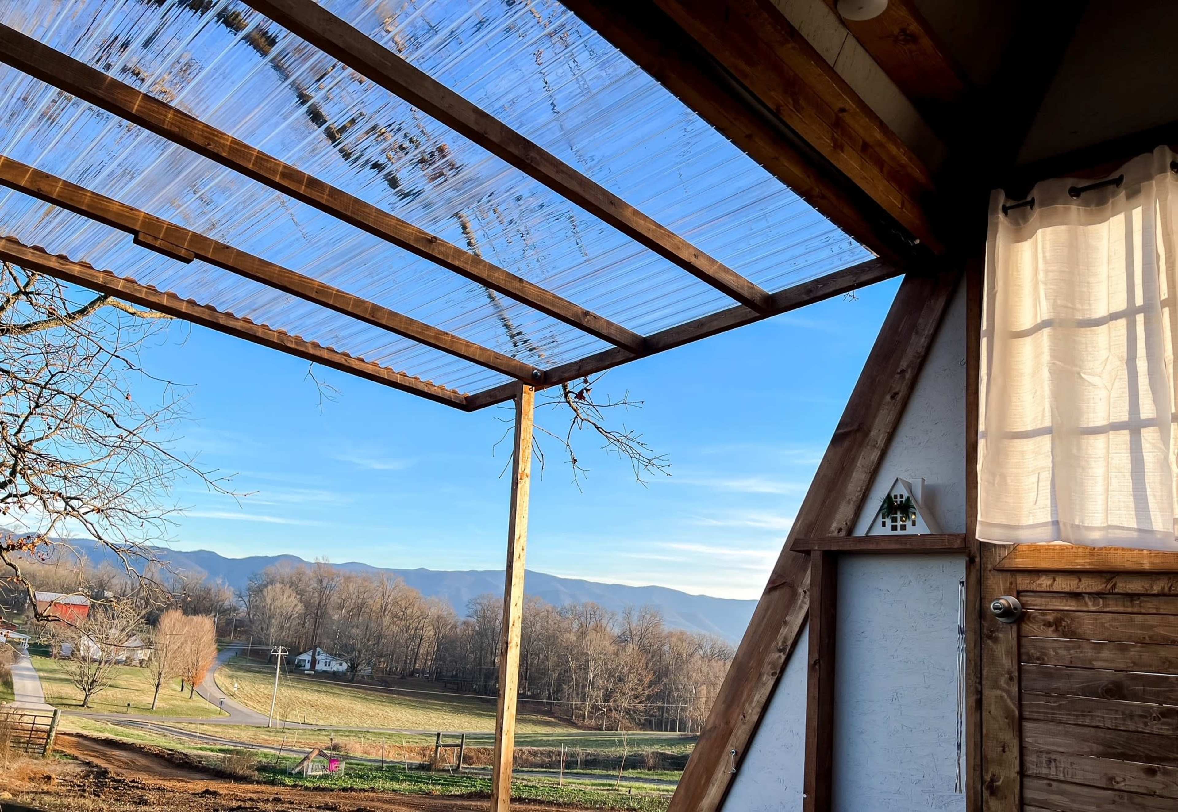 An outdoor space with a clear roof, leading to a view of mountains and fields under a blue sky.