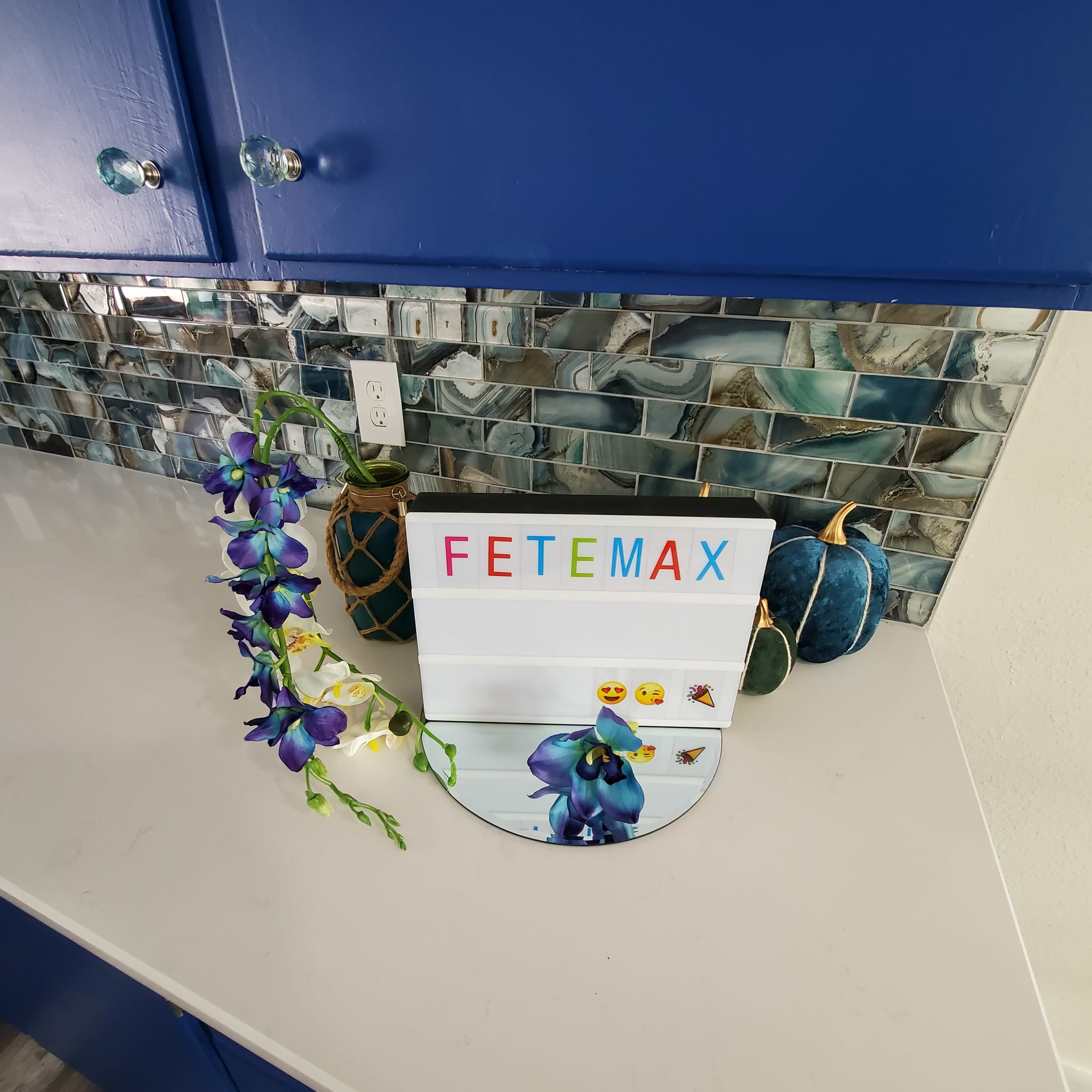 A colorful sign reading "FETEMAX" is displayed on a countertop next to decorative pumpkins and an orchid.