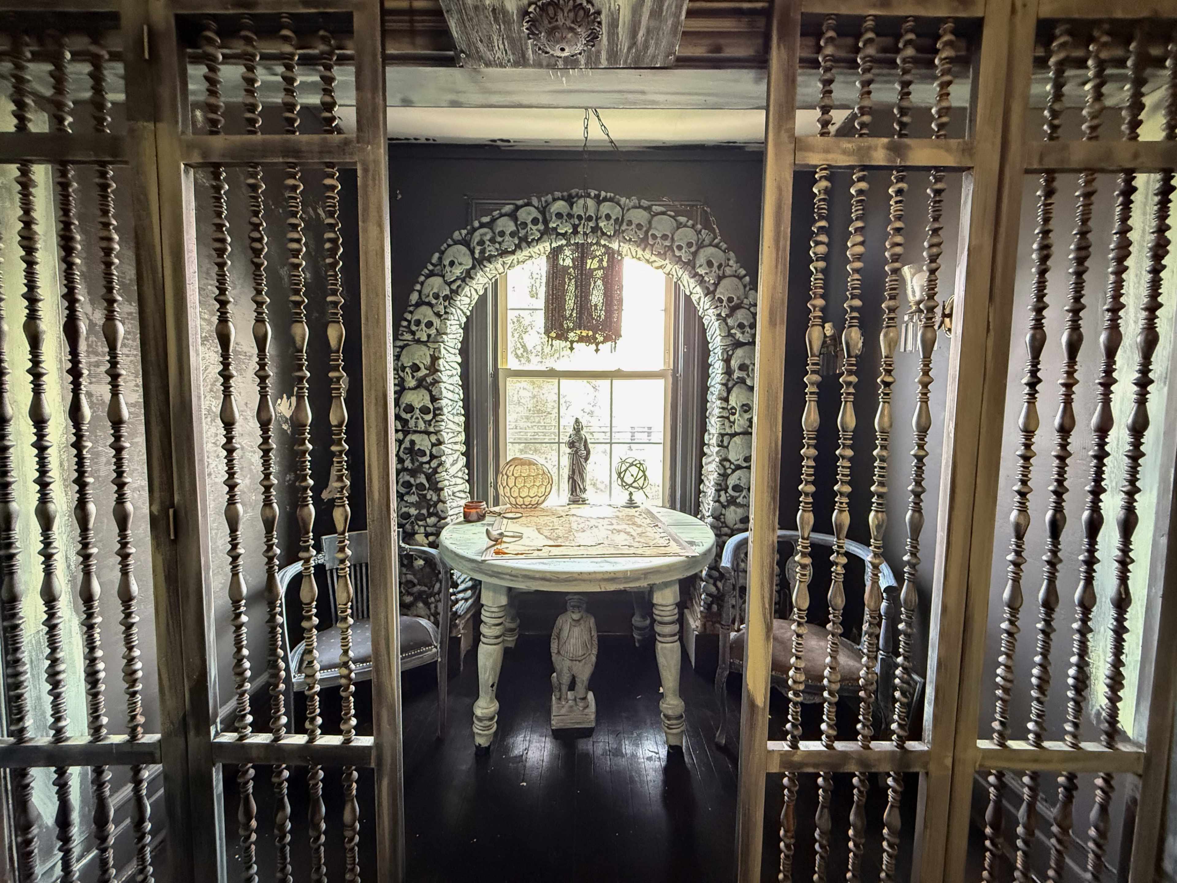 The image shows a small dining area enclosed by wooden screens, featuring a round table with decorative elements and a window adorned with intricate patterns.