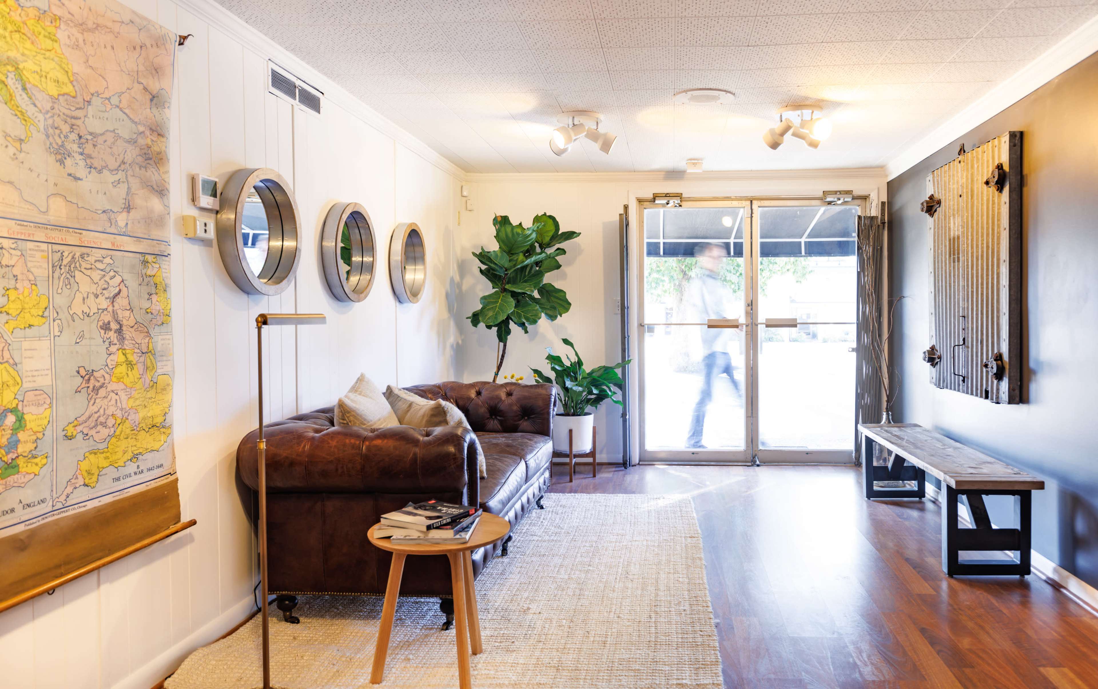 A cozy entryway with a leather couch, a potted plant, mirrors on the wall, and a wooden bench near a glass door.
