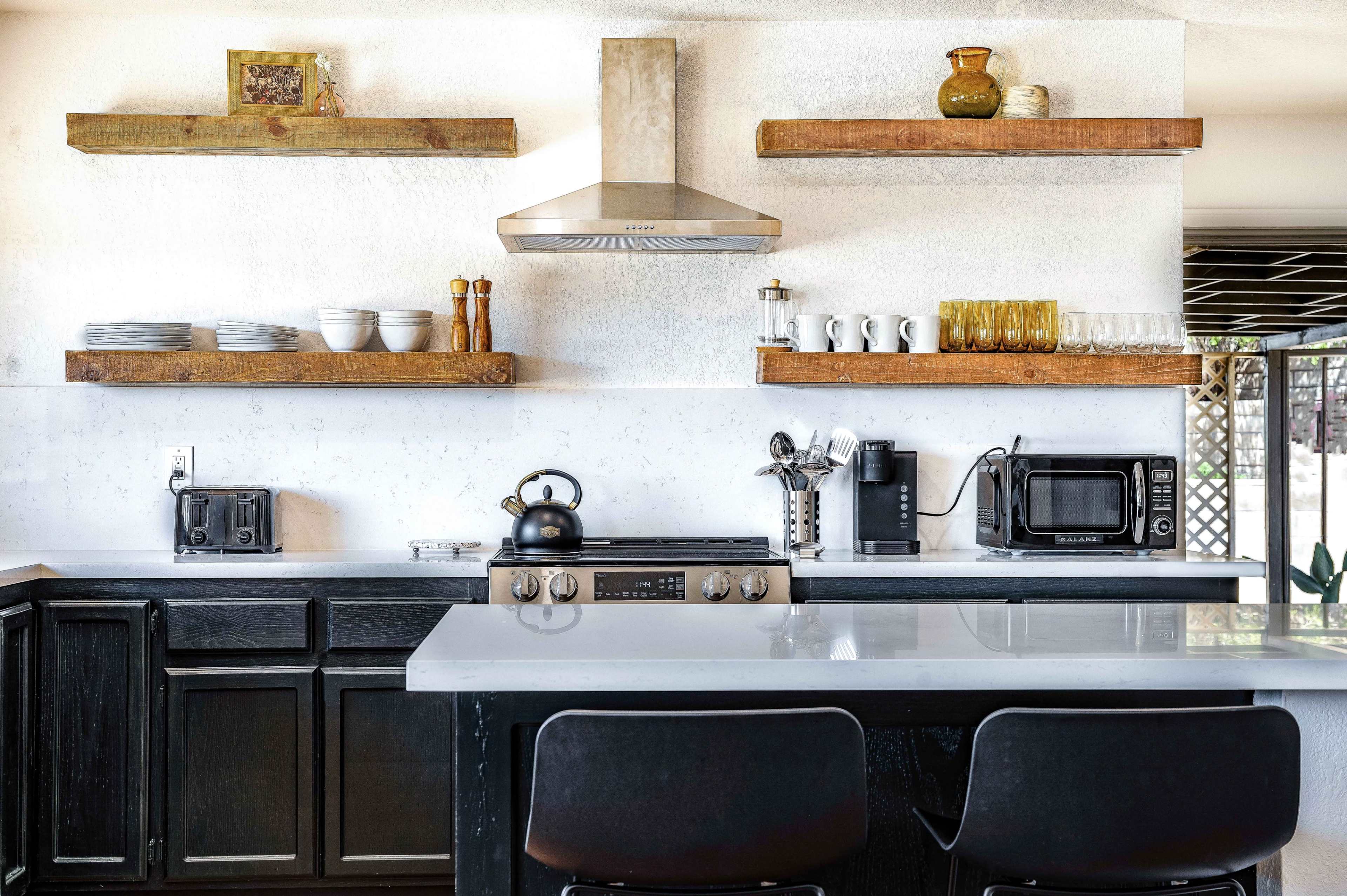 A modern kitchen with dark cabinets, a central island, and wooden shelves displaying various kitchen items and appliances.