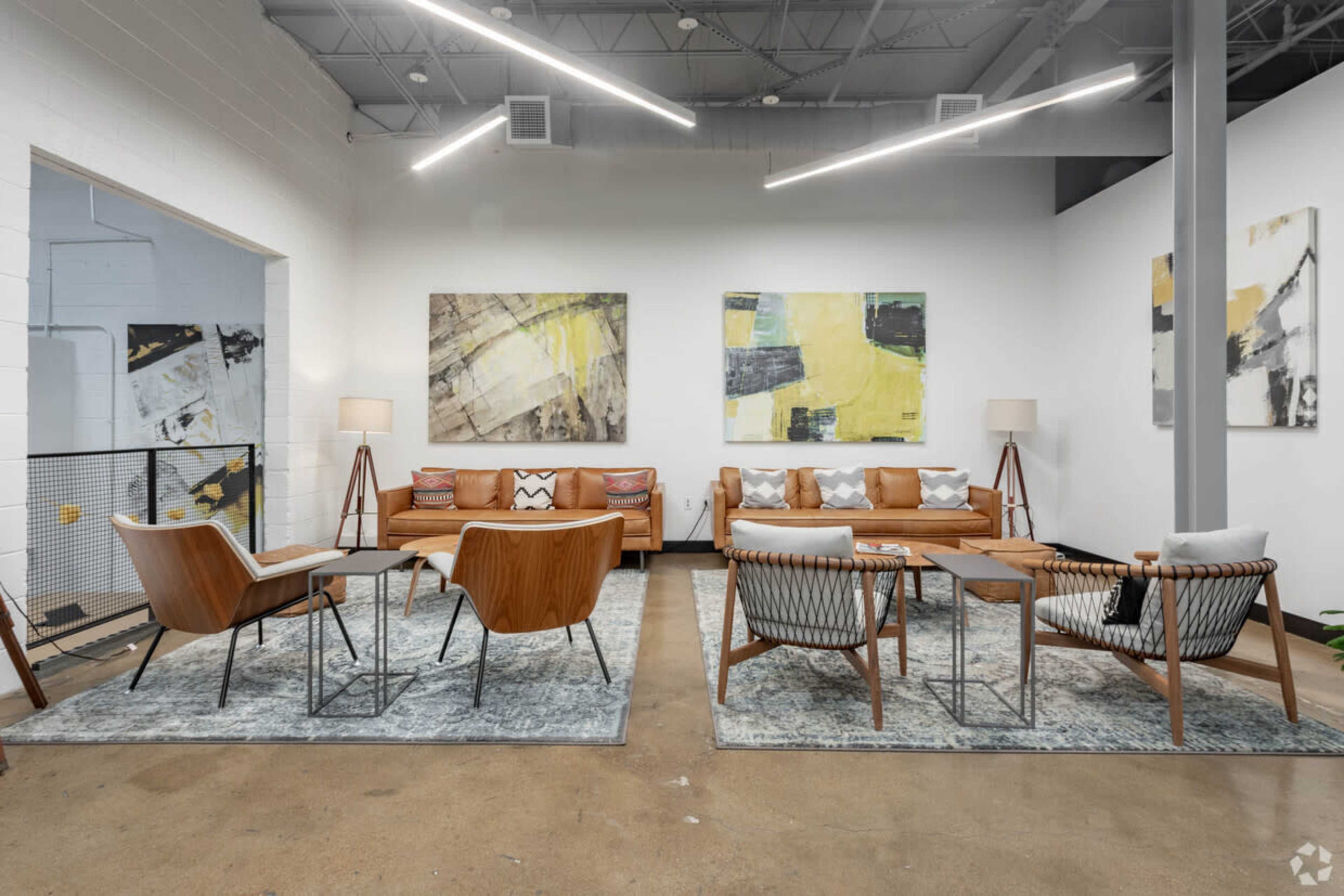 A modern interior space featuring two leather sofas, several armchairs, coffee tables, abstract wall paintings, and a polished concrete floor.