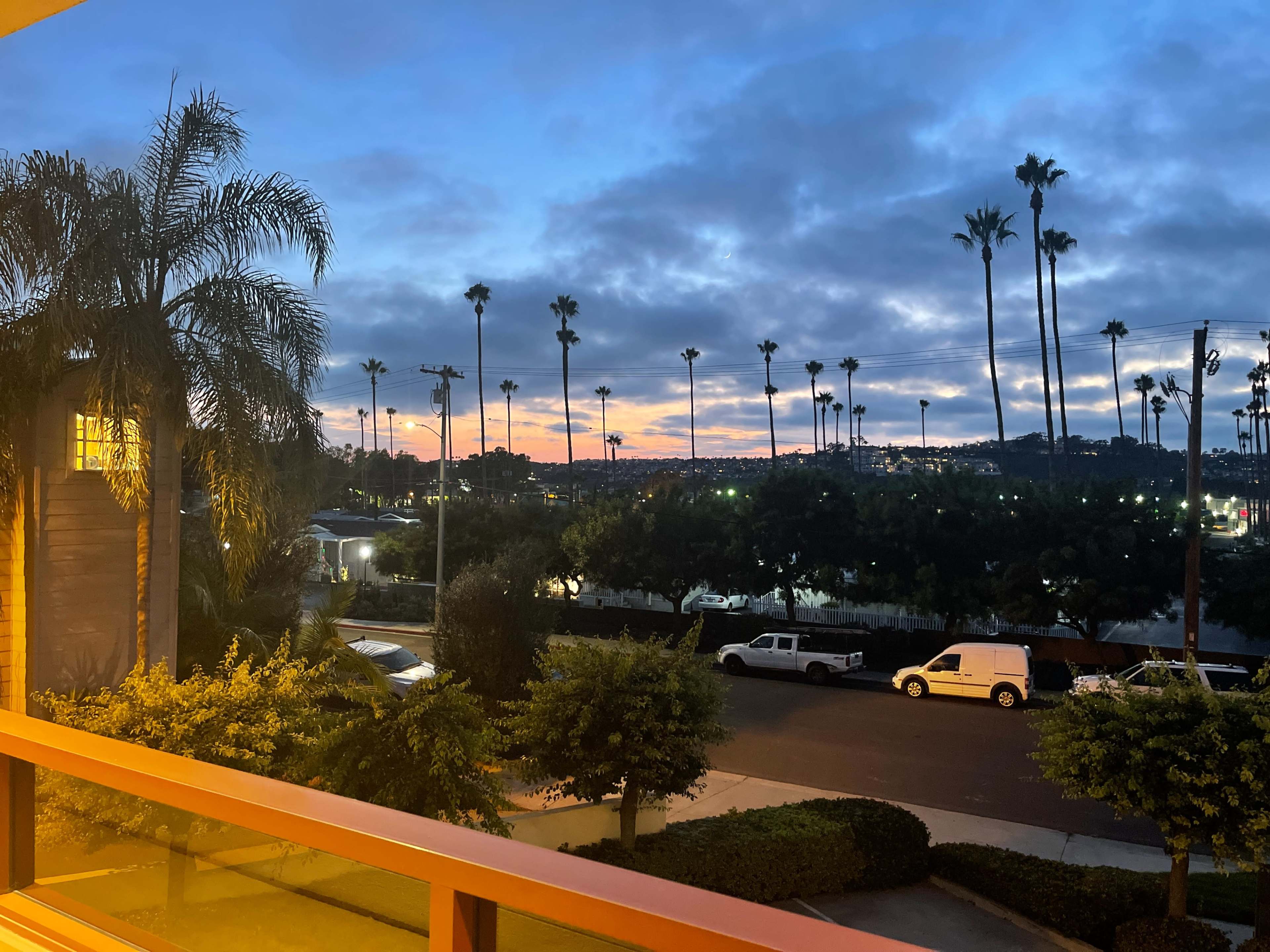 A coastal sunset view with palm trees silhouetted against a colorful sky, and a street scene with parked vehicles.