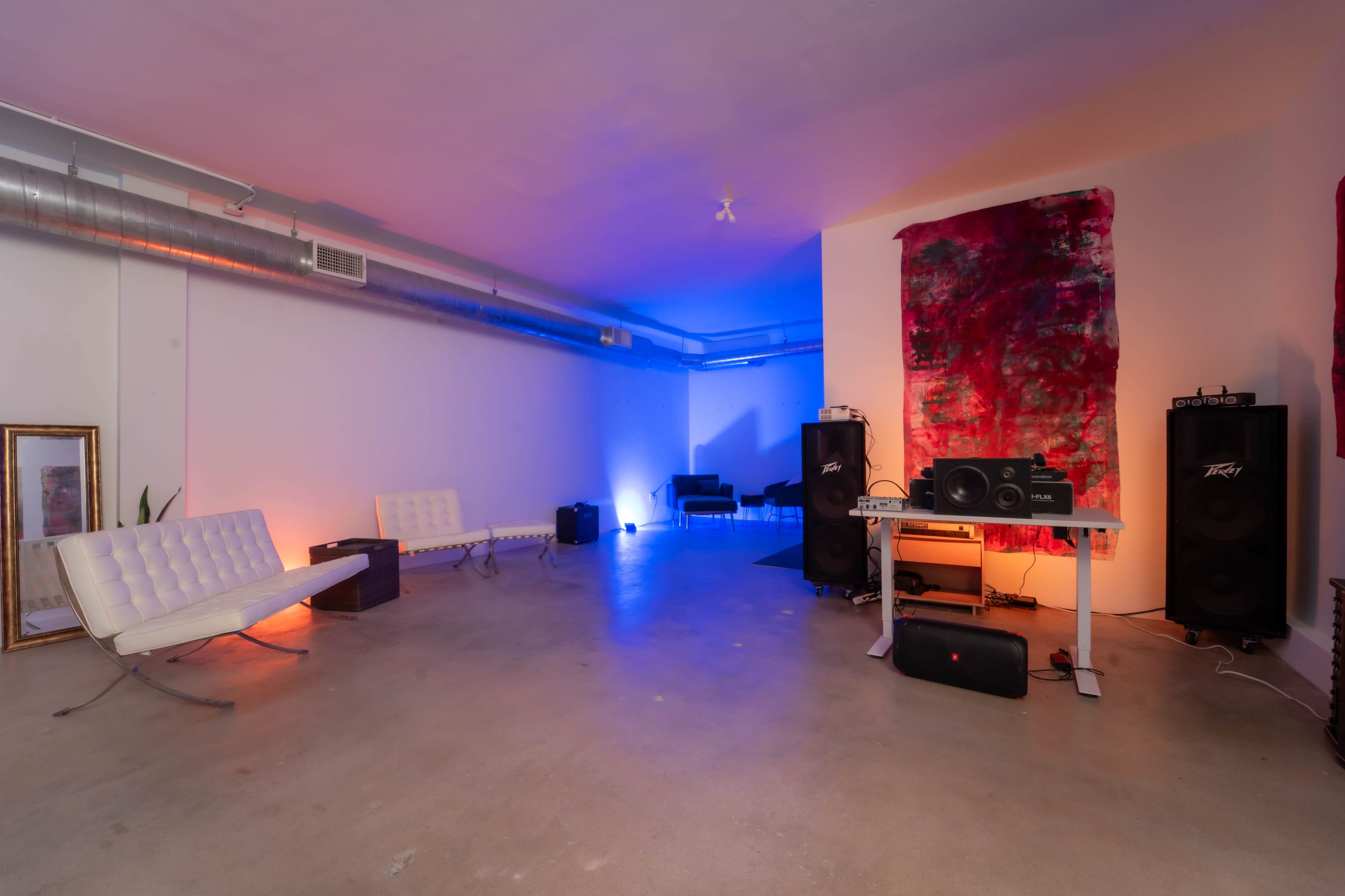 A spacious room features minimalist white furniture, colorful lighting, and audio equipment set up for a music setting.
