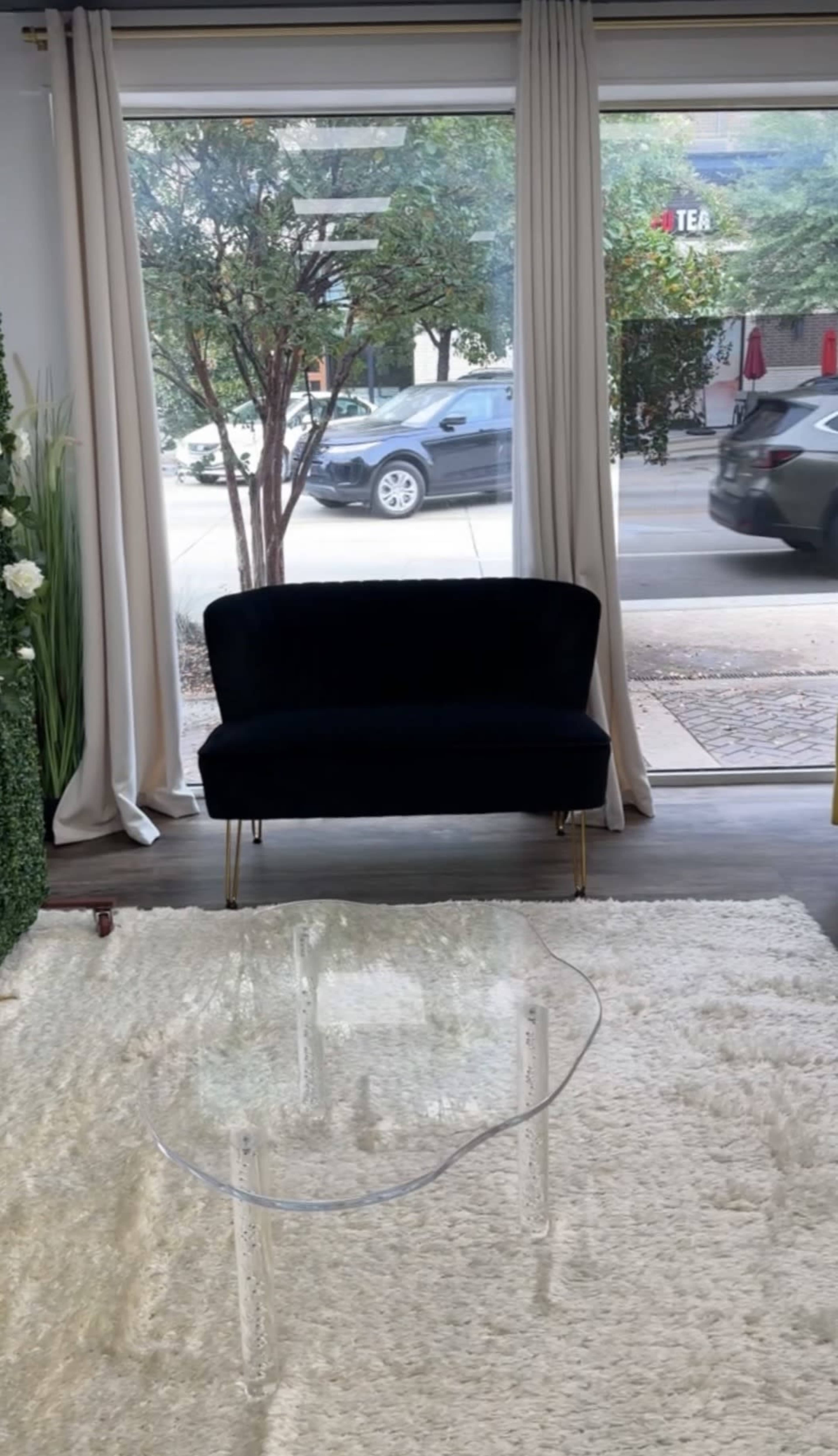 A dark velvet sofa sits in front of large windows with sheer curtains, overlooking a street with a passing car.