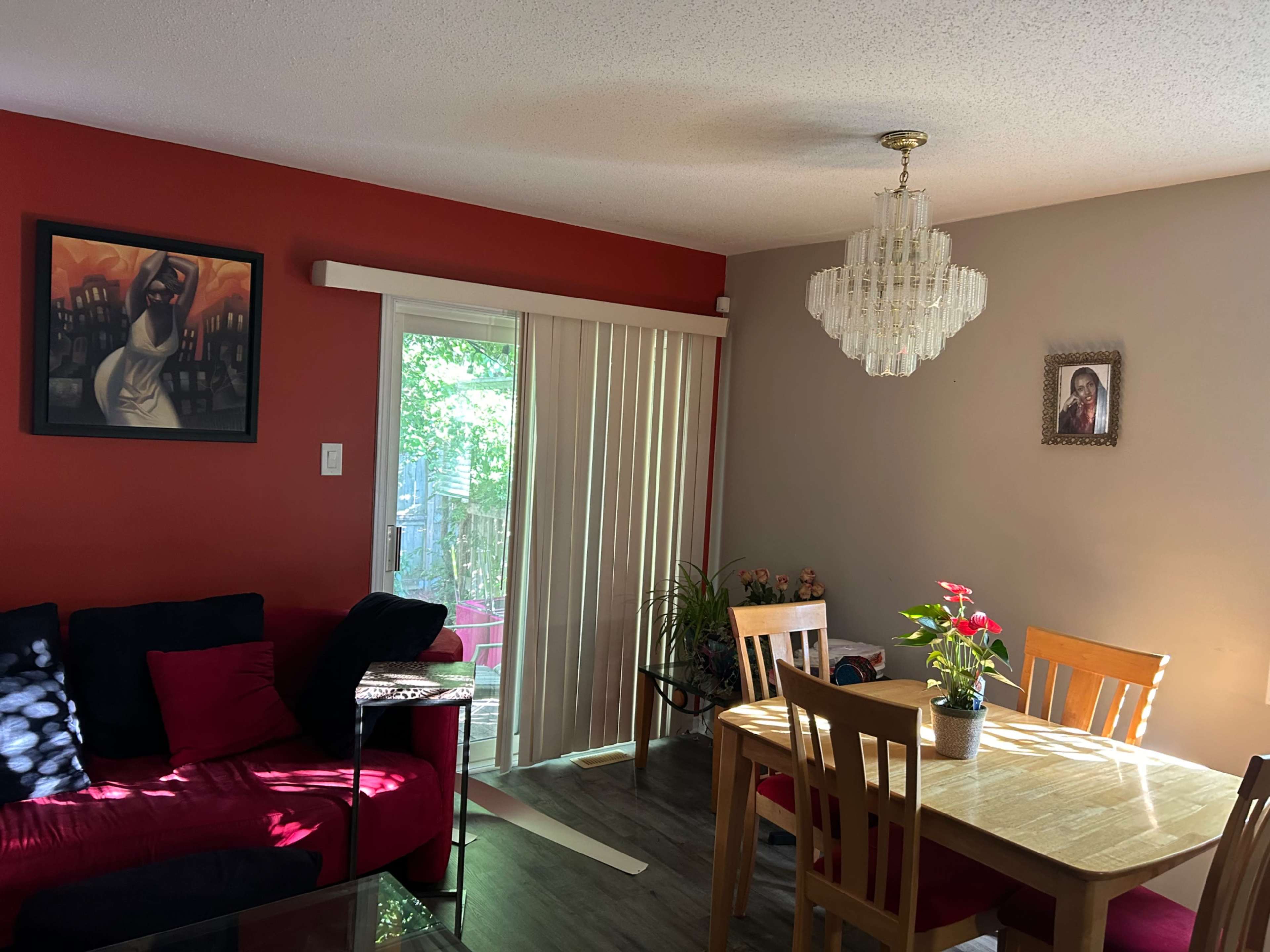 A living room with a red accent wall, a dining table, sliding glass doors, and artwork on the walls.