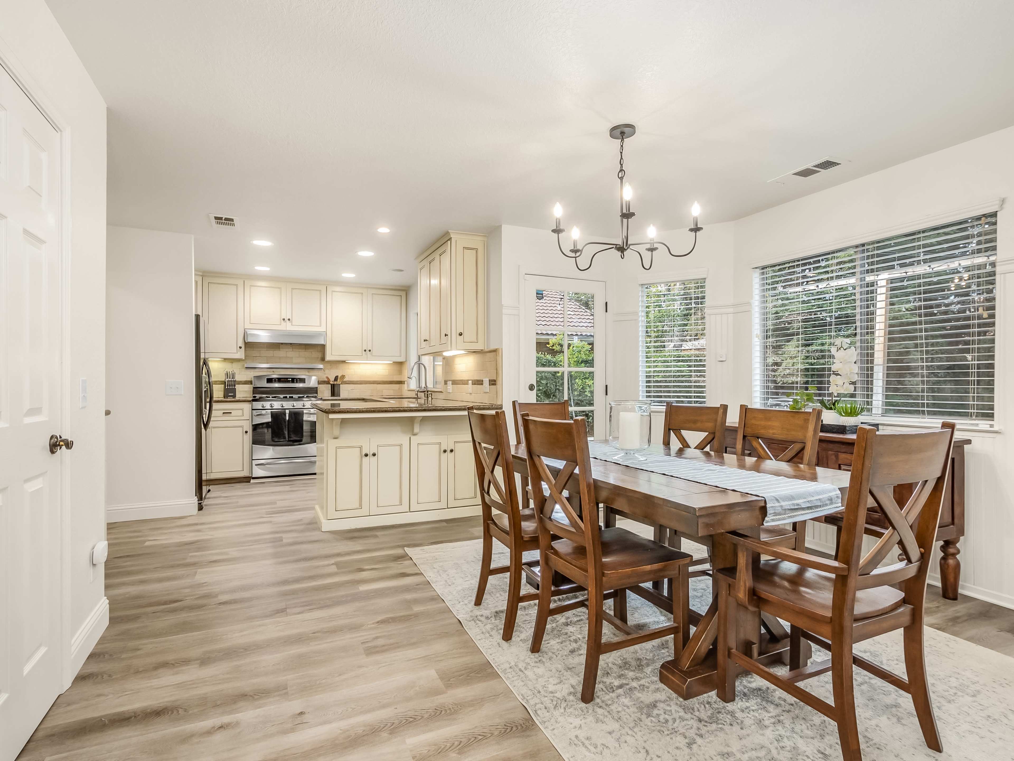 A spacious dining area features a wooden table surrounded by six chairs, with a kitchen visible in the background.