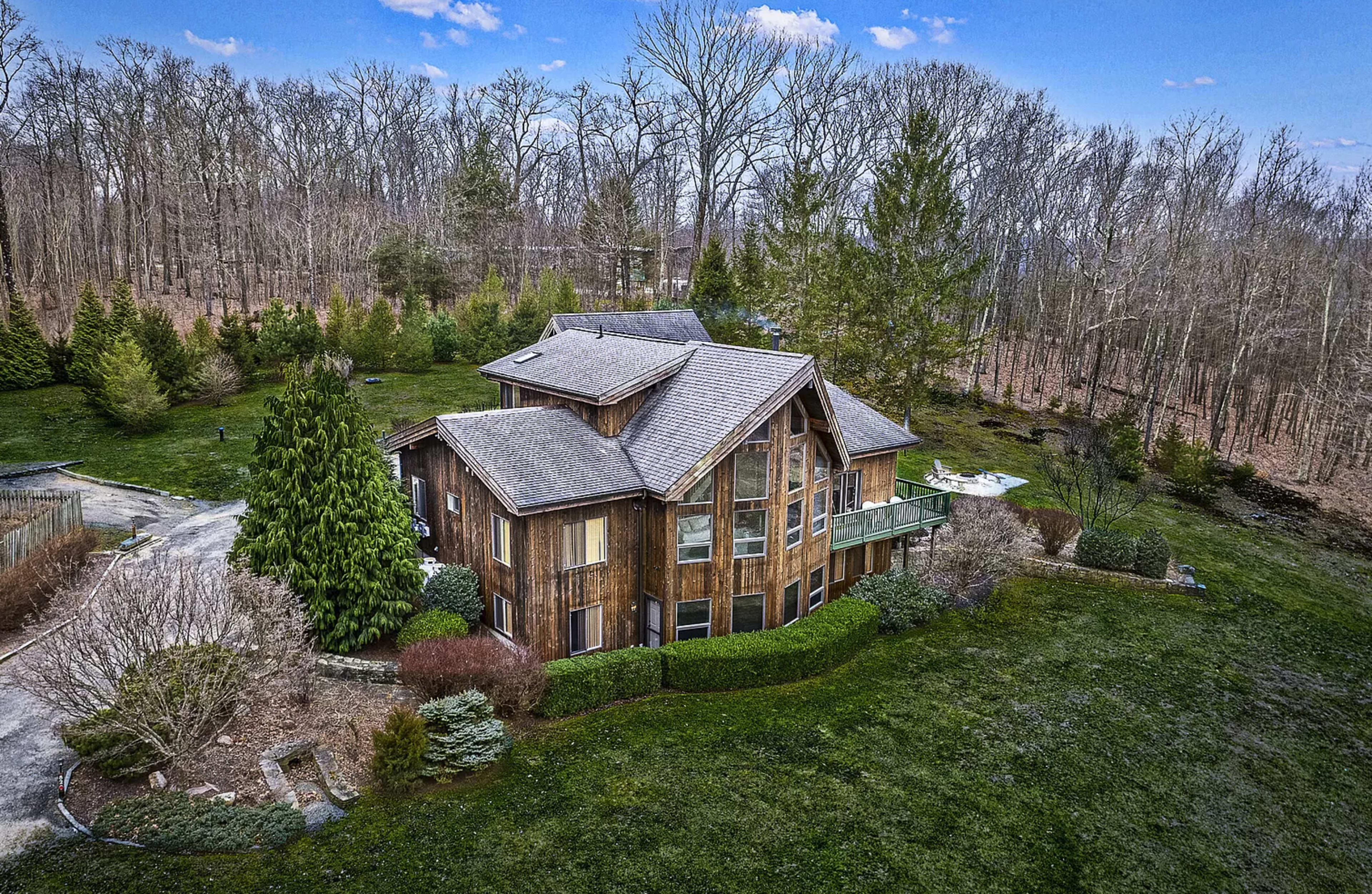 A large wooden house with large windows is situated on a grassy property surrounded by trees.