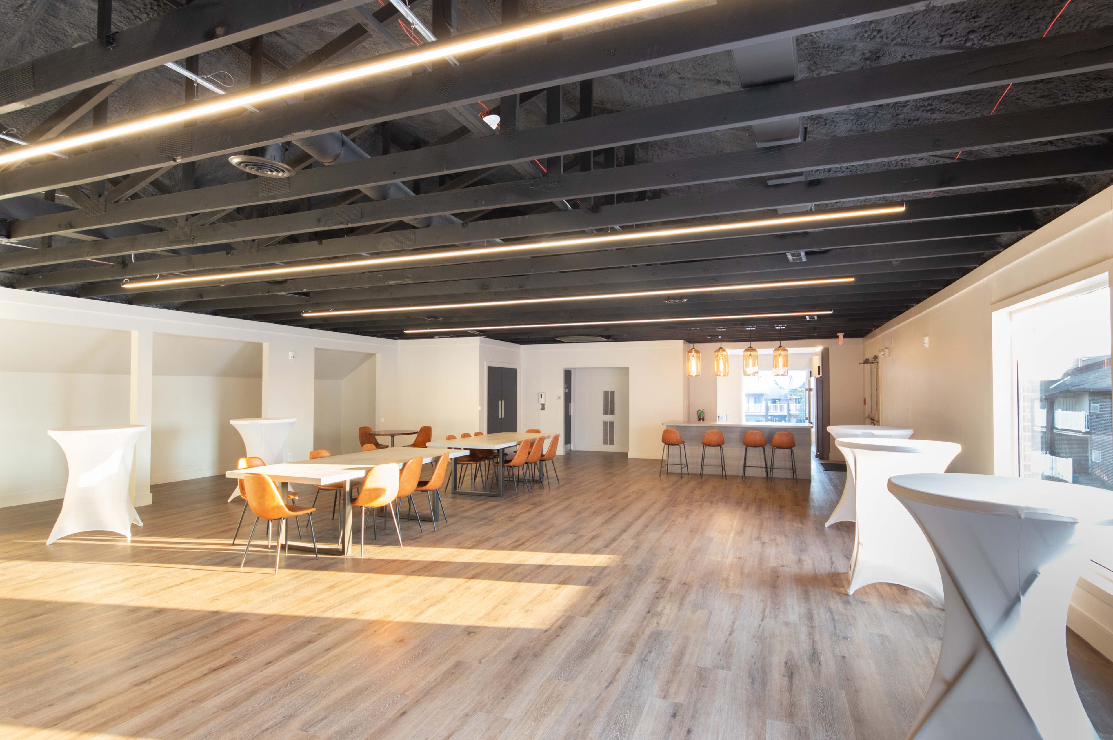 A spacious, modern event room with wooden flooring, tables and chairs arranged for seating, and a series of pendant lights.