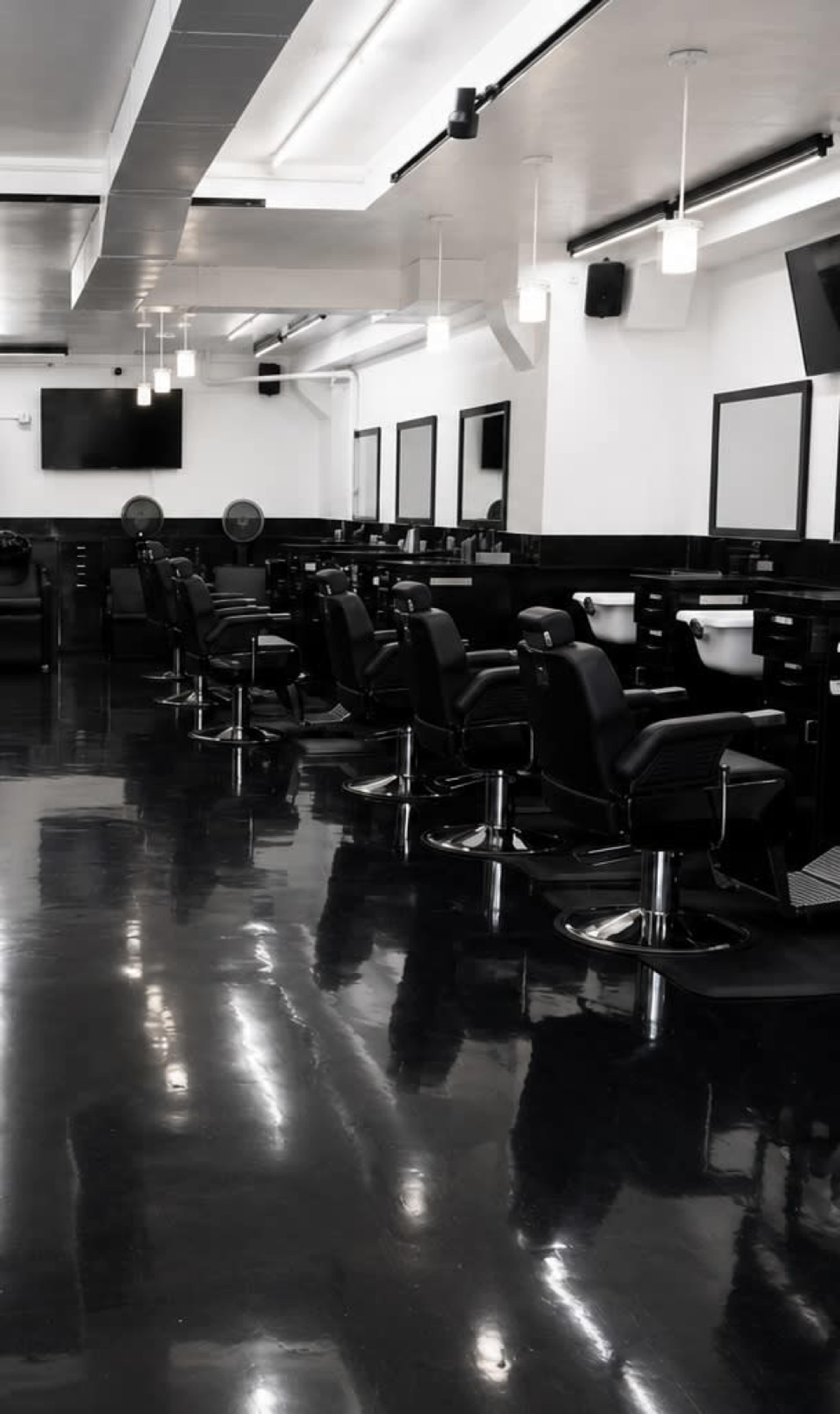 The image shows an empty barbershop with black styling chairs and glossy flooring, illuminated by overhead lights.