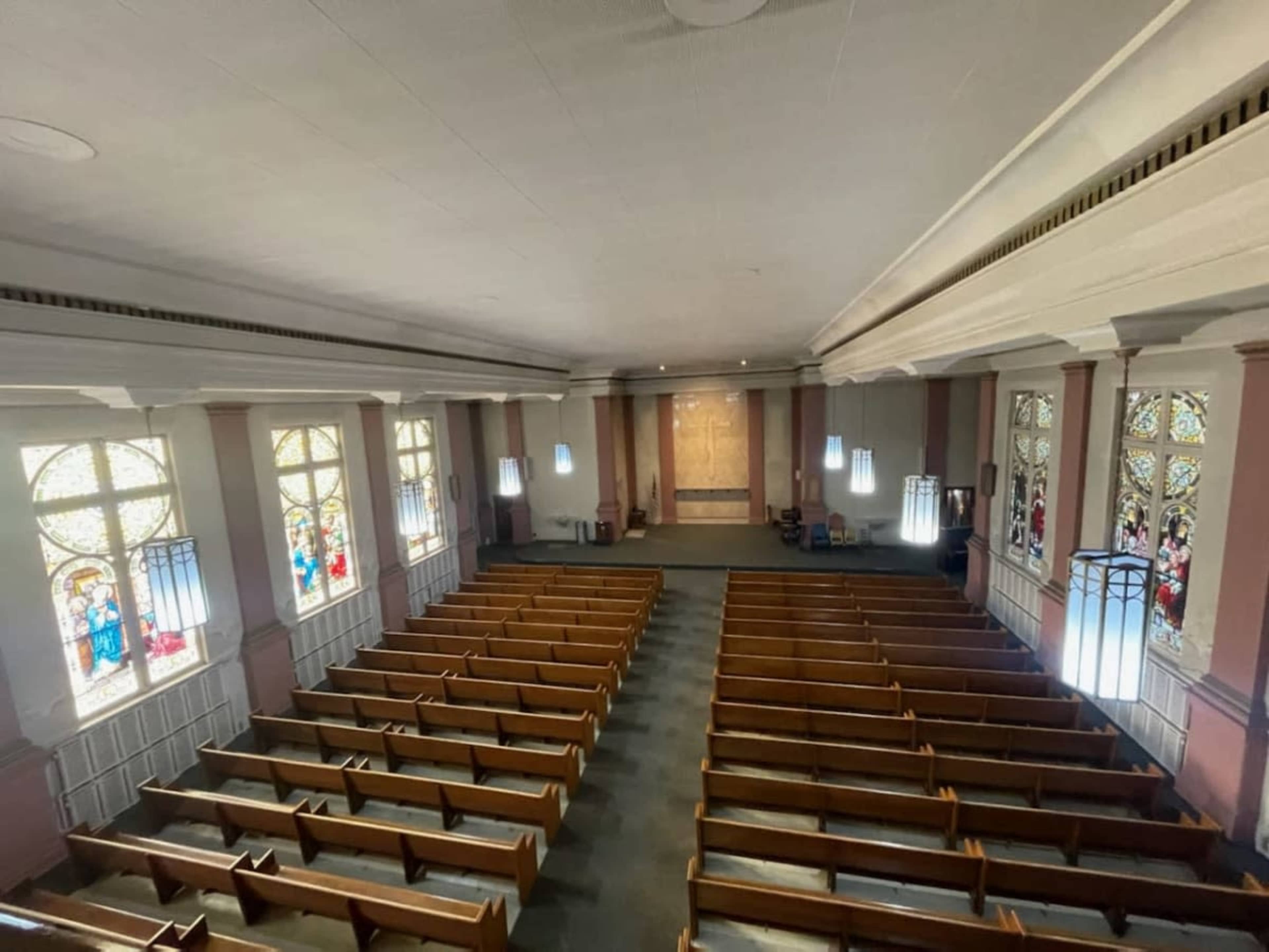 The interior of a church with rows of wooden pews and stained glass windows.