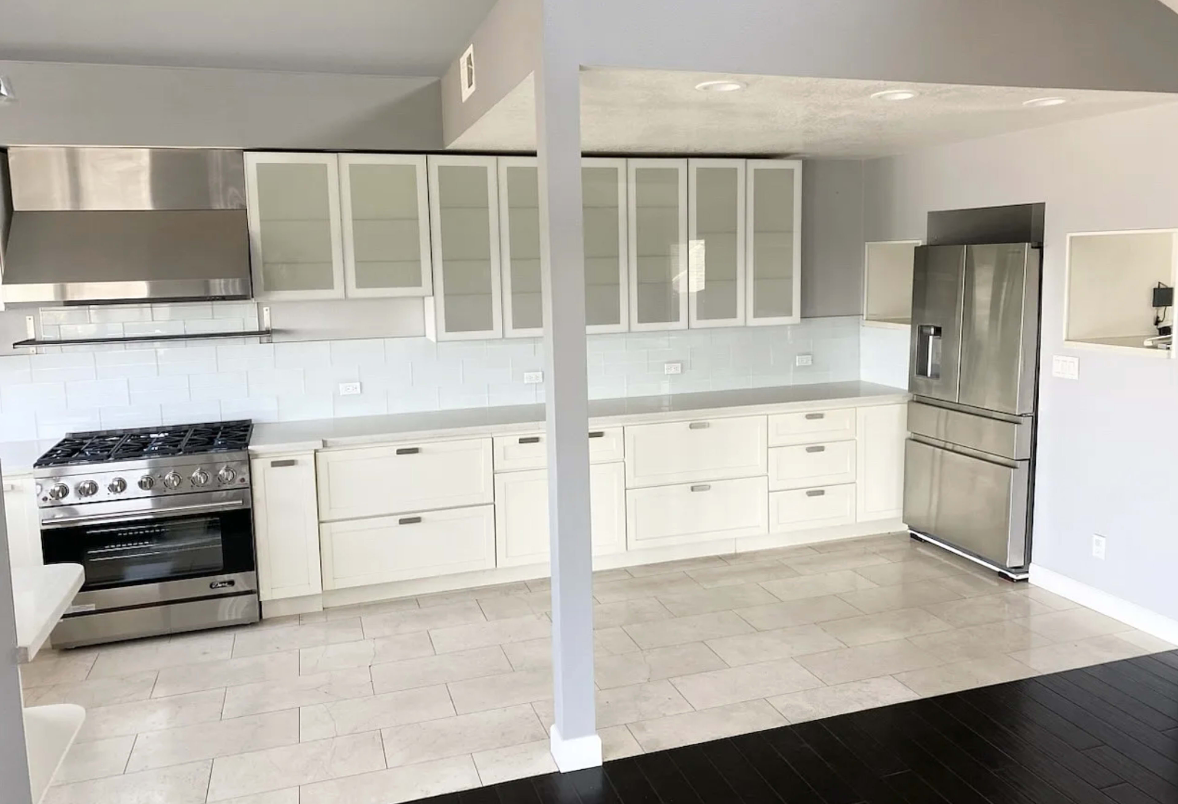 The image shows a modern kitchen with white cabinetry, stainless steel appliances, and a tile floor.