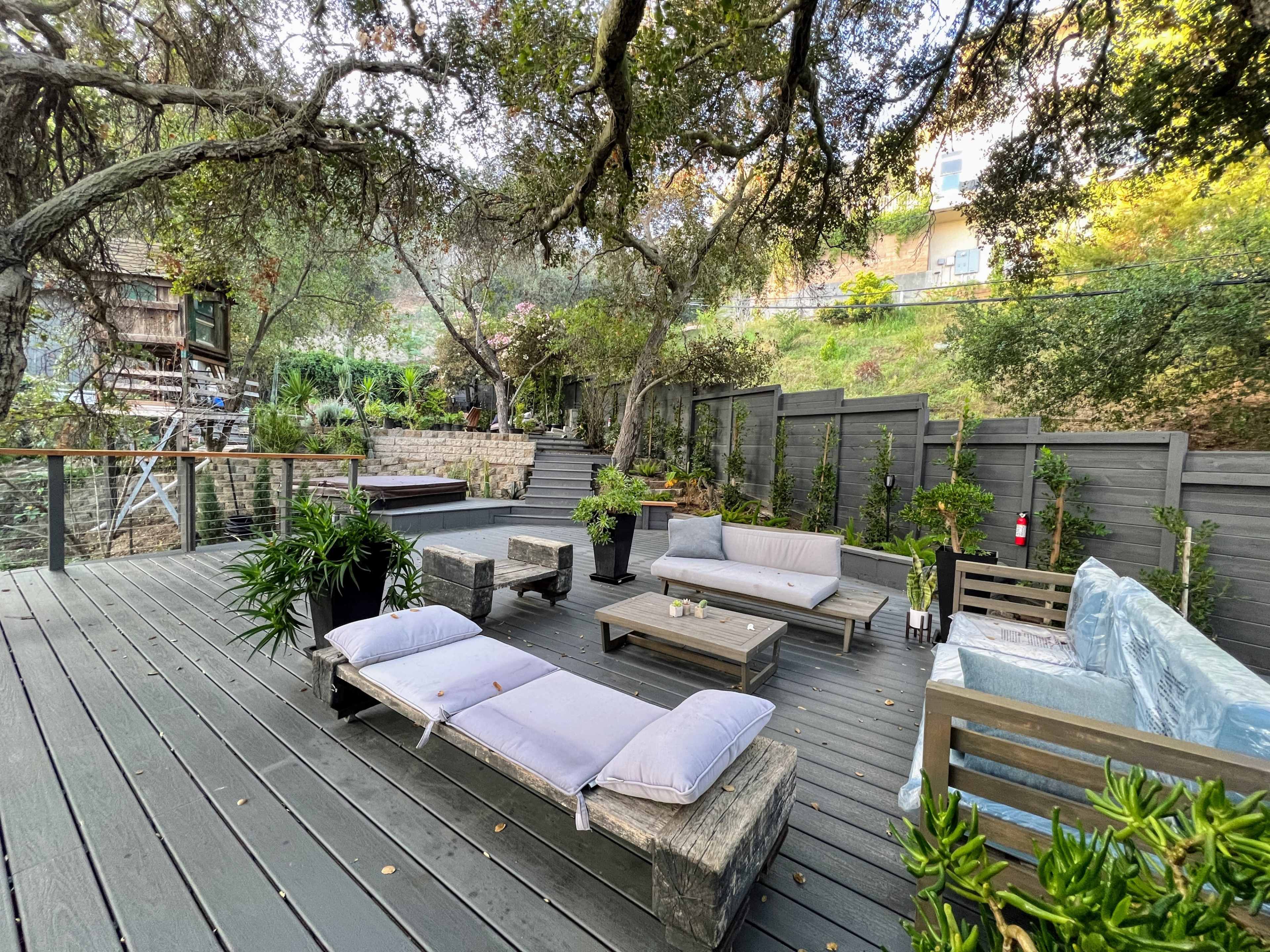 A wooden deck area with several seating arrangements and planters surrounded by trees and greenery.