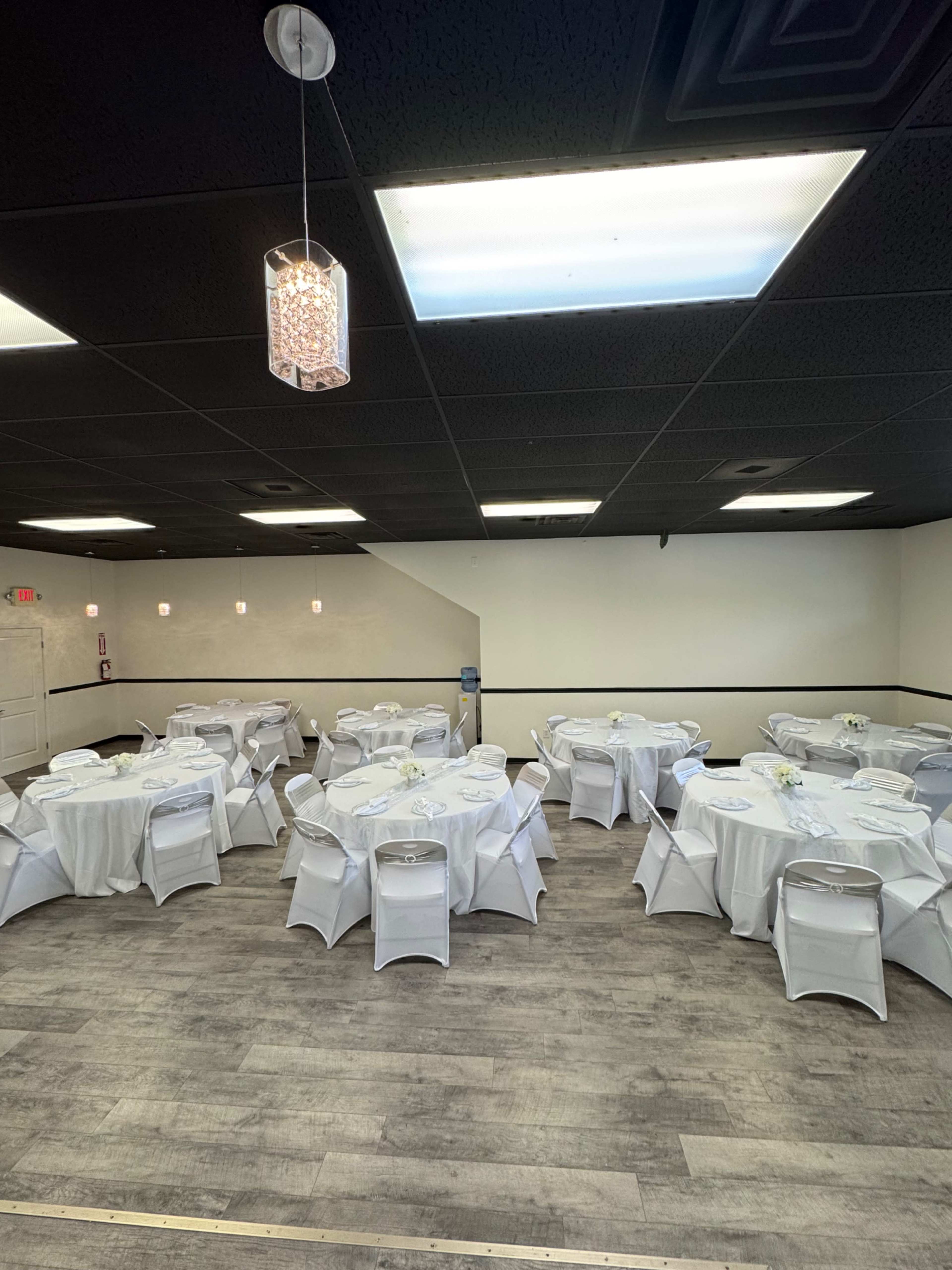 The image shows a banquet hall with several round tables covered in white tablecloths, each adorned with a small floral centerpiece.