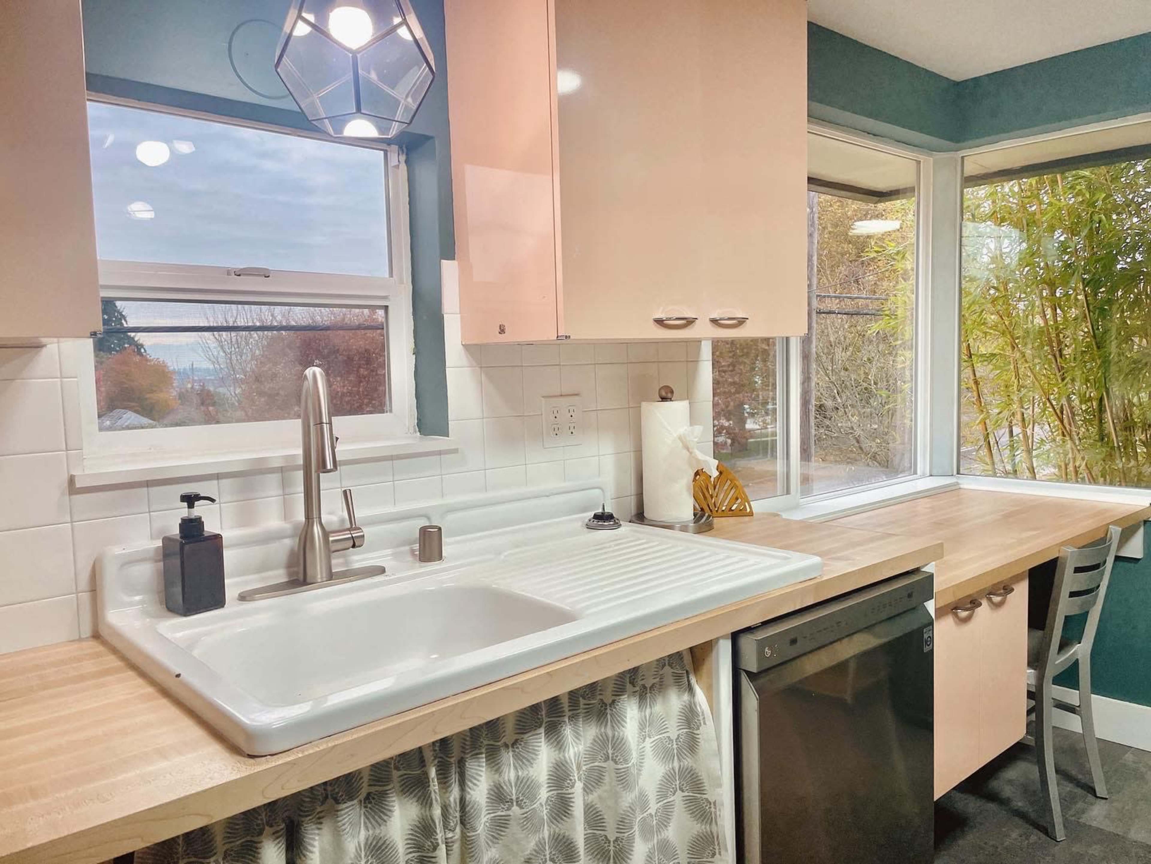A modern kitchen features a double sink with a window view, light-colored cabinets, and a wooden countertop by a dining area.