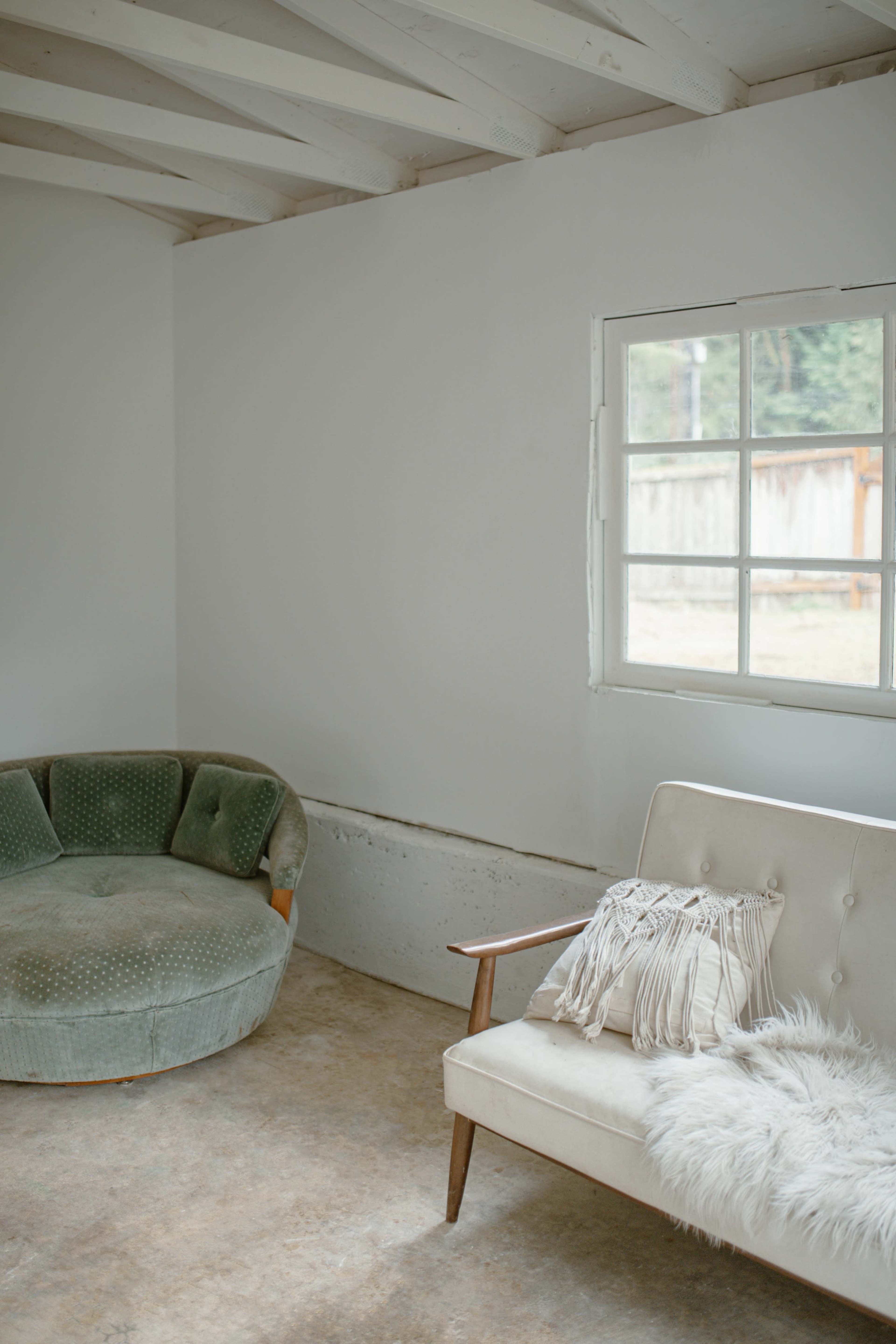The image shows a minimalist room with a green circular sofa and a white two-seater couch beside a window.